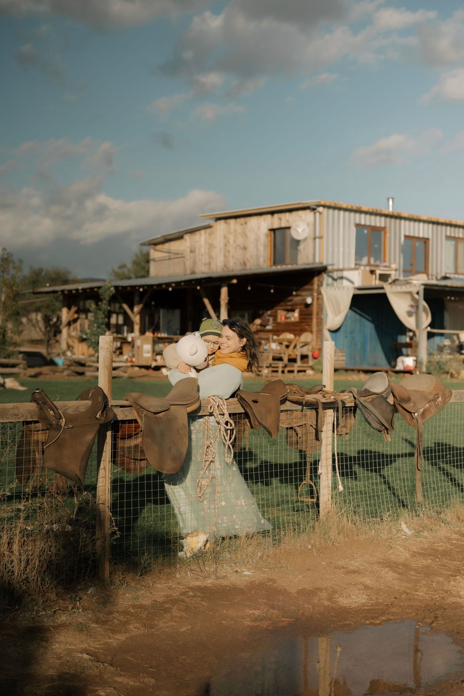 A row of rustic scarecrows stand guard along a wire fence at a rural farm under cloudy skies.