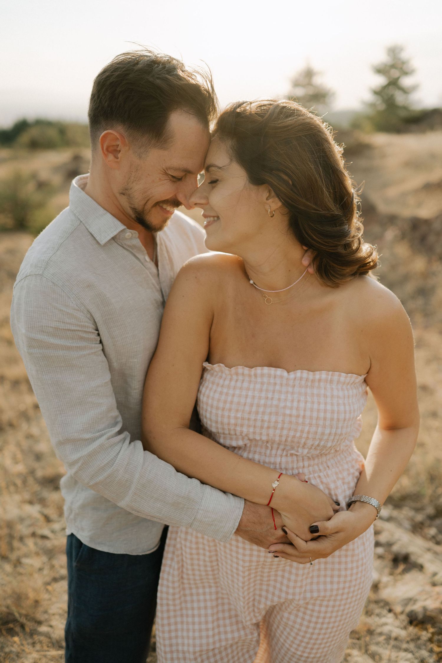 A couple shares intimate moments in a desert setting during golden hour while wearing gray and gingham outfits.