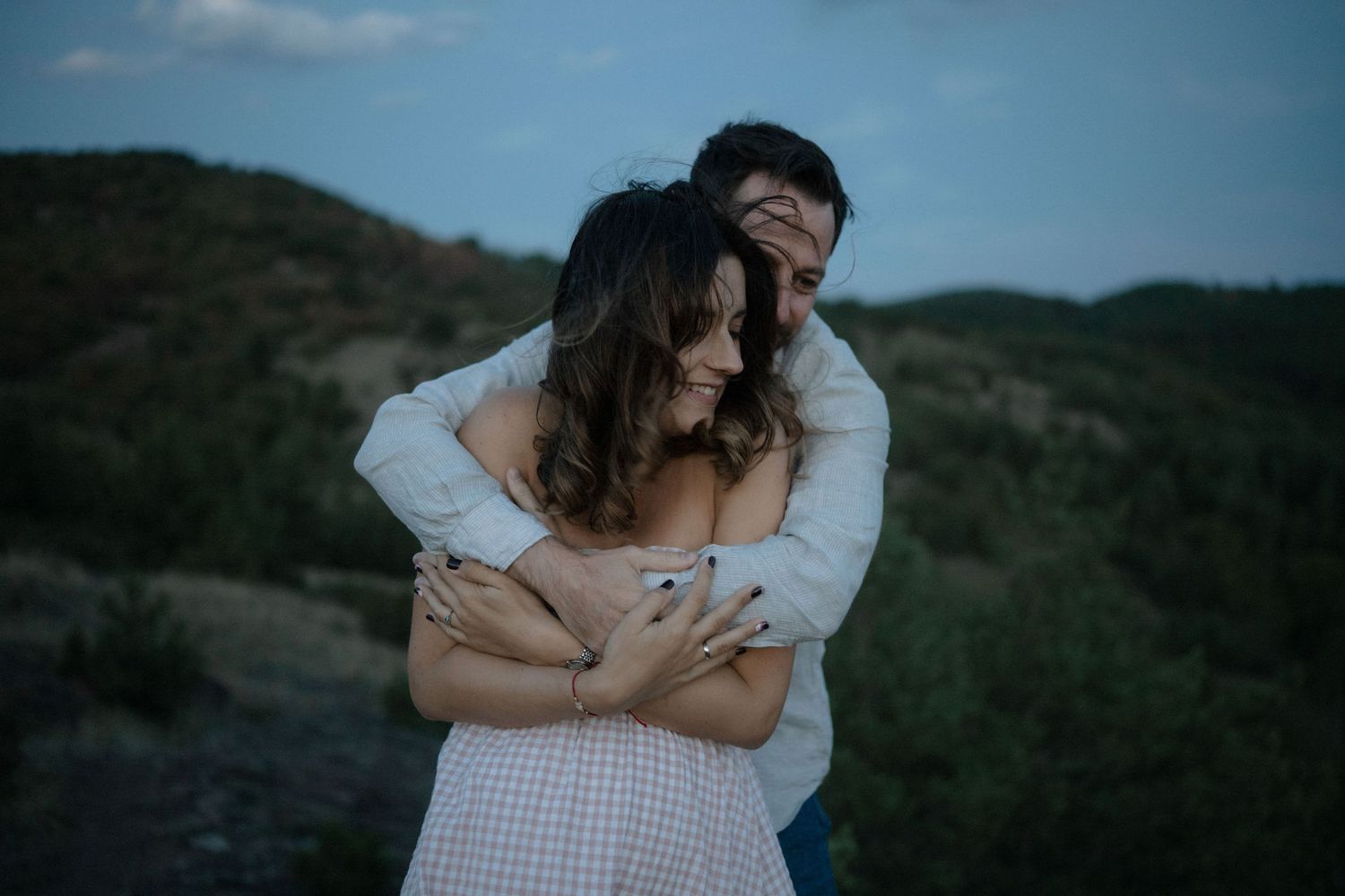 A couple embraces tenderly on a hillside during sunset, creating a romantic silhouette against the darkening sky.
