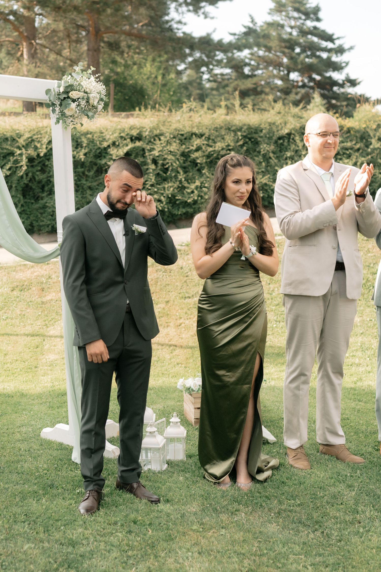 Wedding party members playfully pretend to drink from bottles while posing together on a grassy lawn.