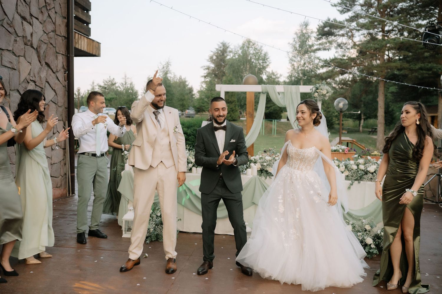 Wedding guests dance in a line during an outdoor reception celebration at sunset.
