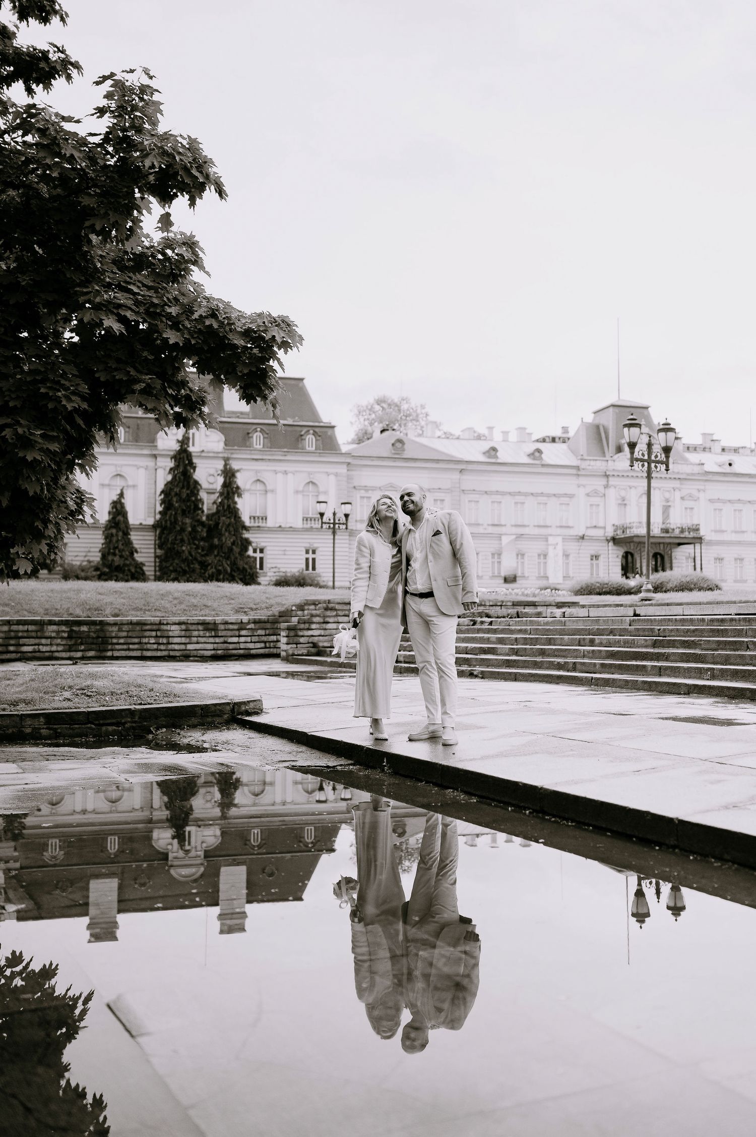 Two people pose artistically near water reflections at an elegant estate.
