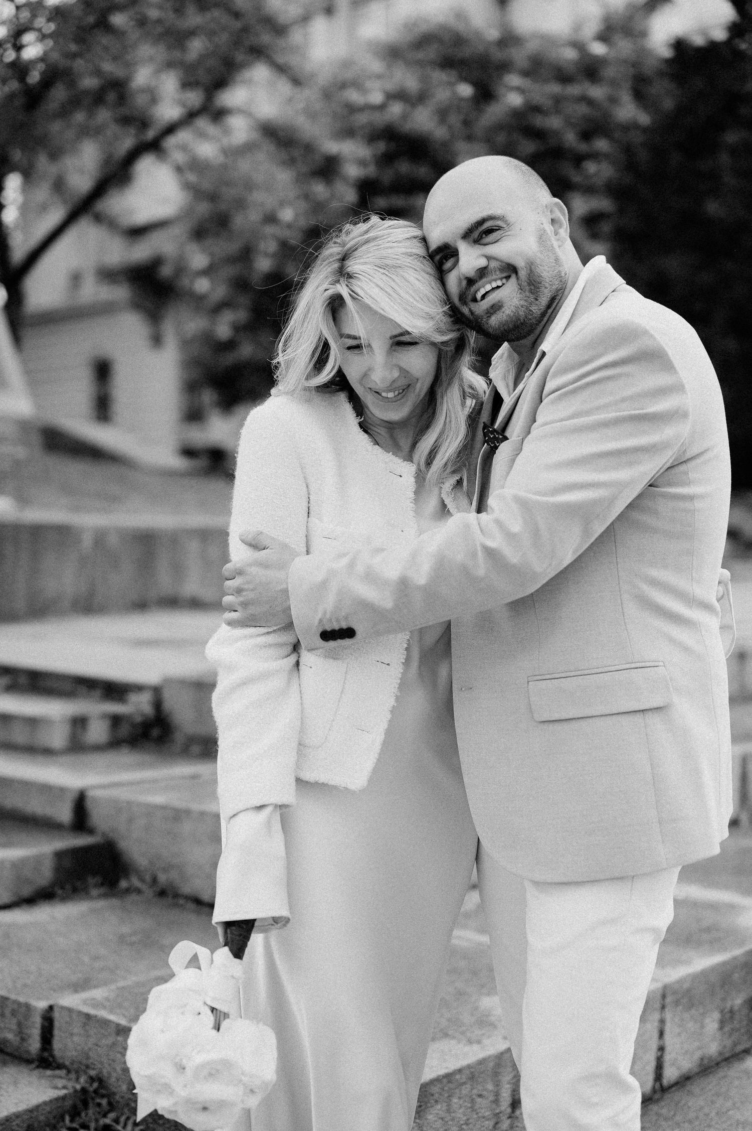 A black and white photo of a couple embracing and laughing together outdoors.