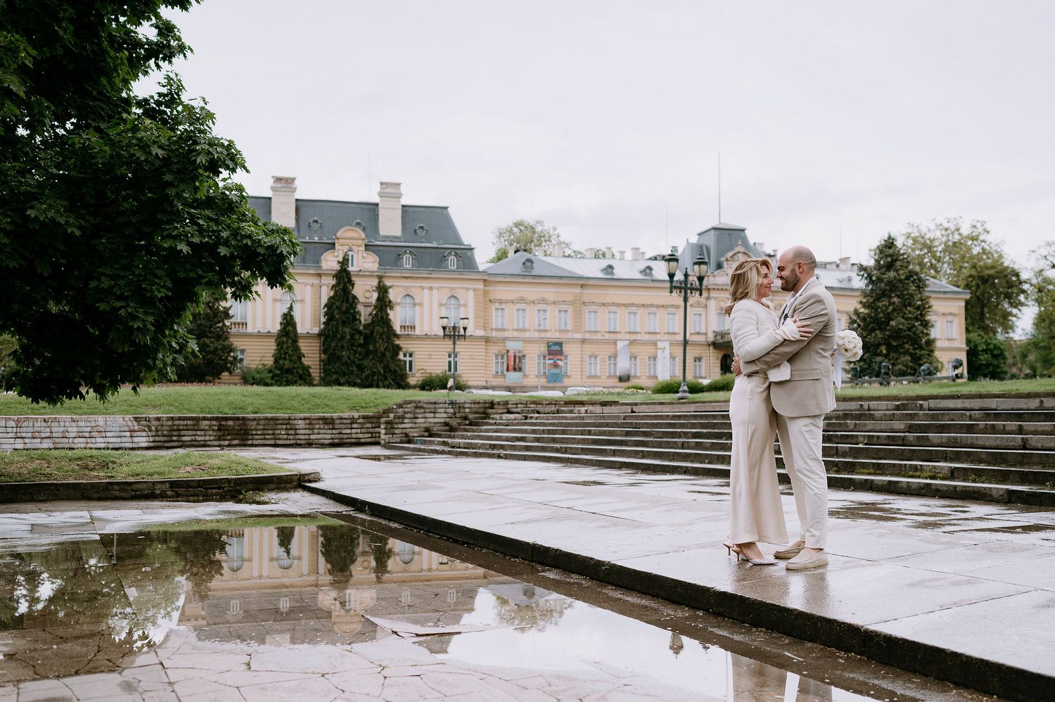 A romantic moment captured near a reflecting pool with classical architecture in the background.