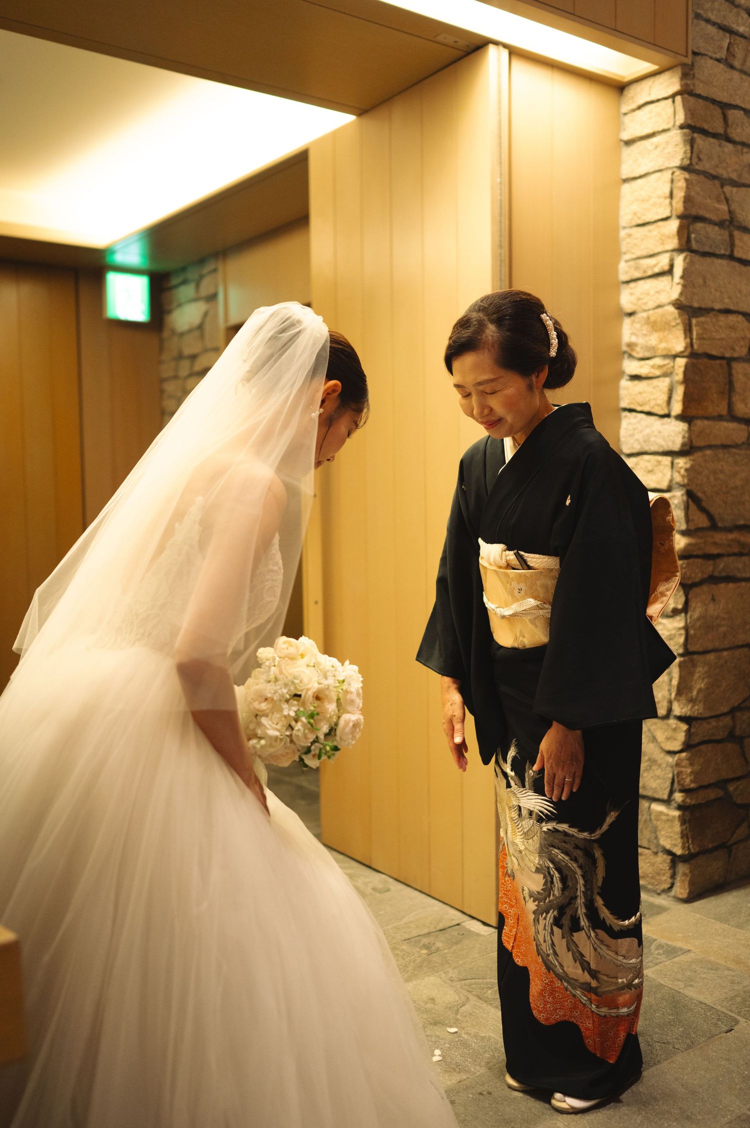 Bride in traditional white dress greets guests in a modern venue hallway.