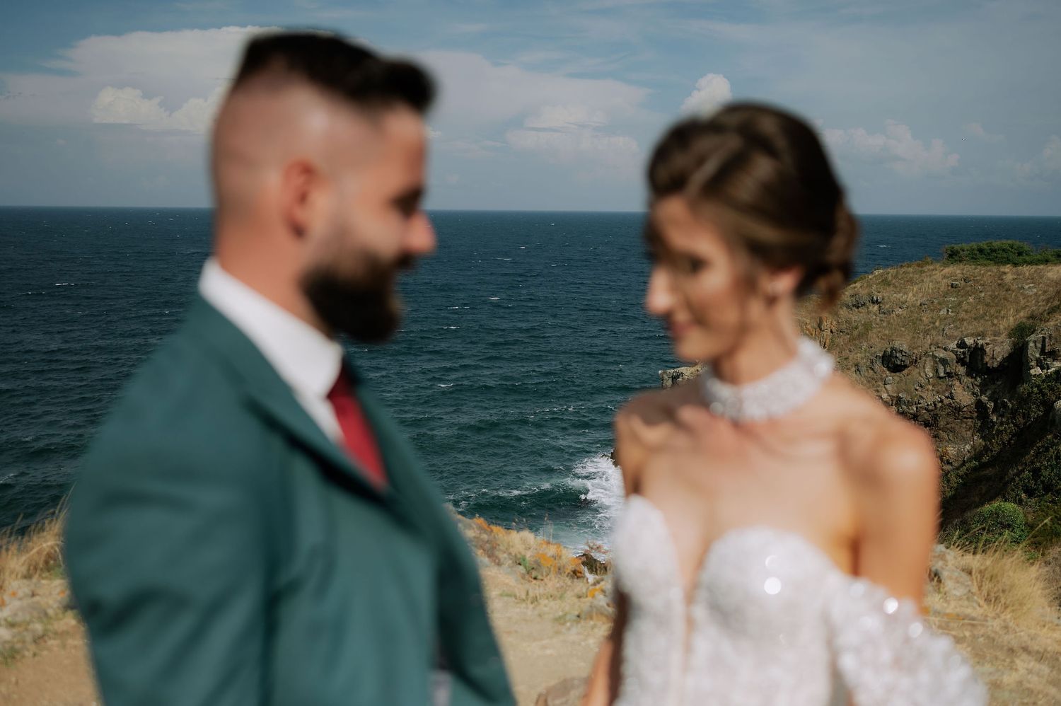 Newlywed couple shares intimate moments against a scenic coastal backdrop with dramatic cliffs and ocean views.