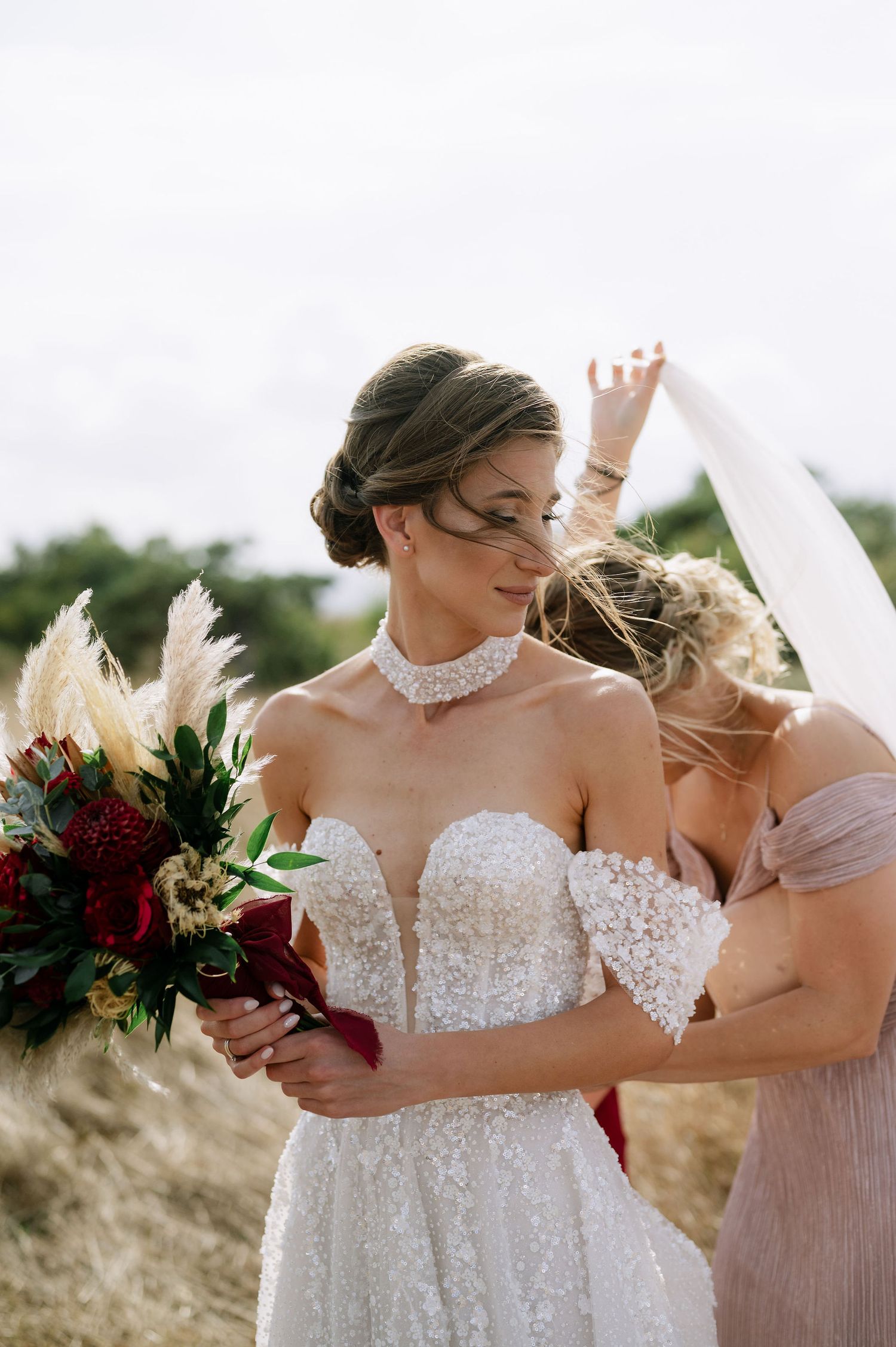 Intimate wedding party moment captured in a sunlit field with floral bouquets.