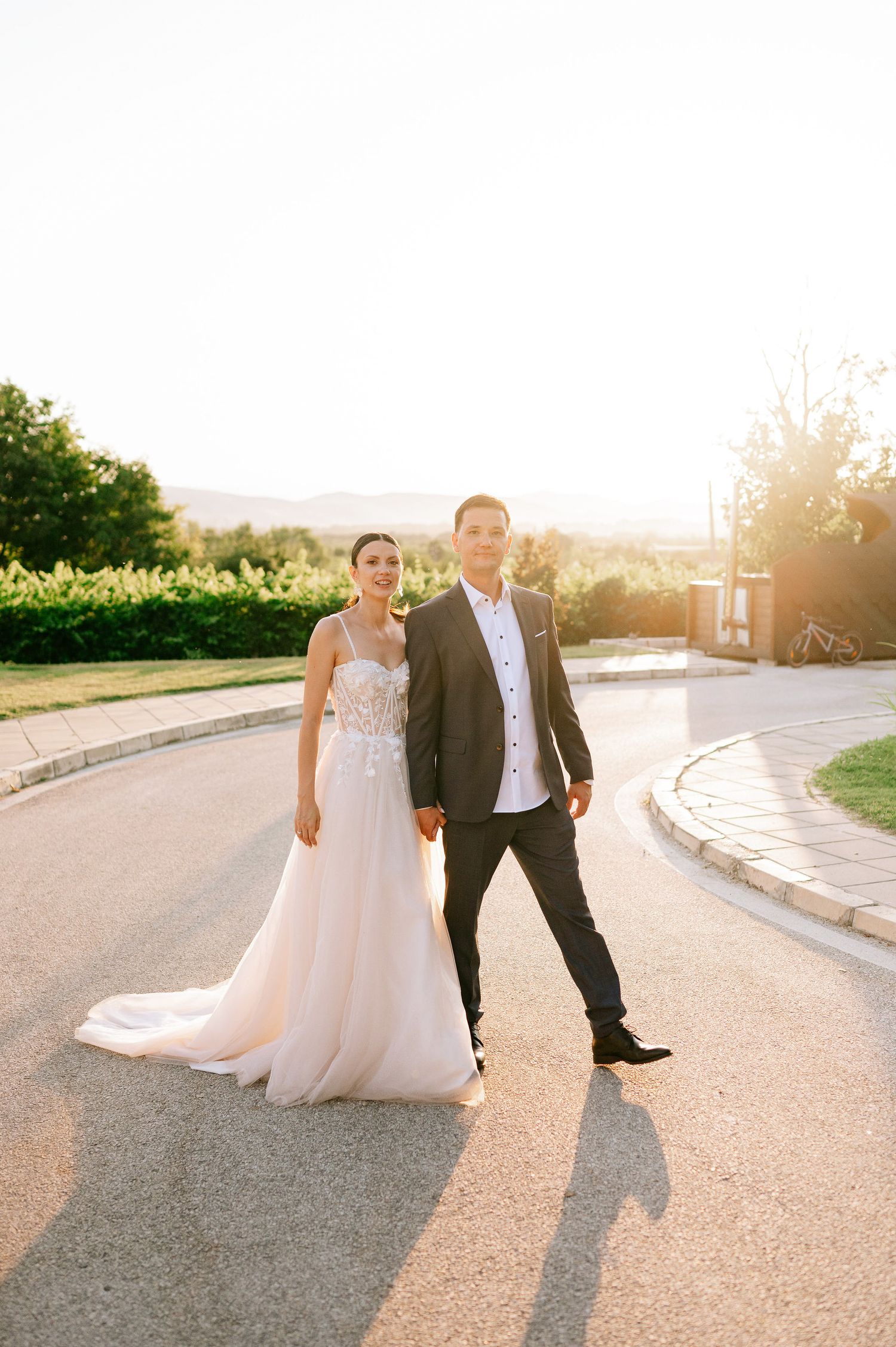 Newlyweds strolling together on a paved pathway during sunset.