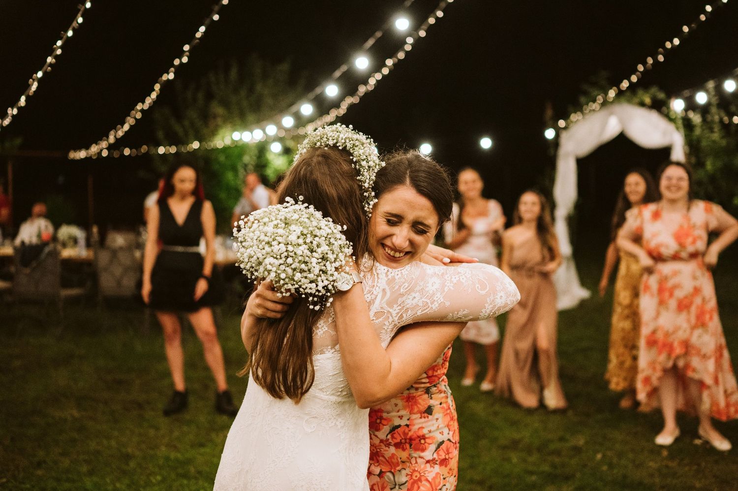 Wedding reception guests dance and celebrate under string lights at dusk.