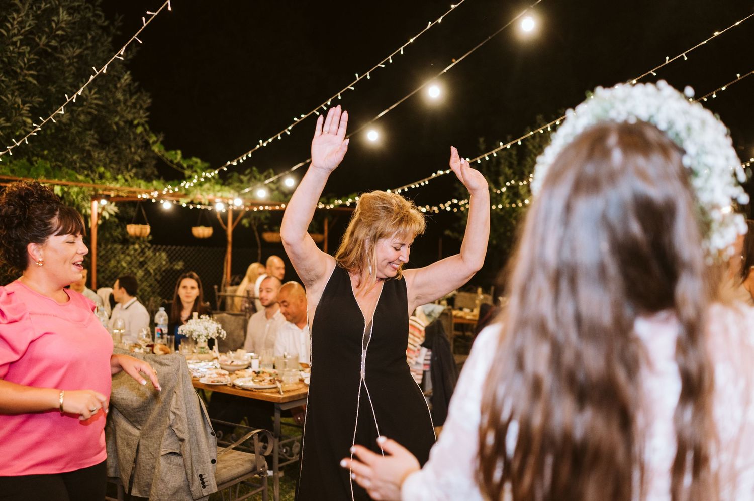 Wedding guests dancing and celebrating under string lights at an outdoor evening reception.