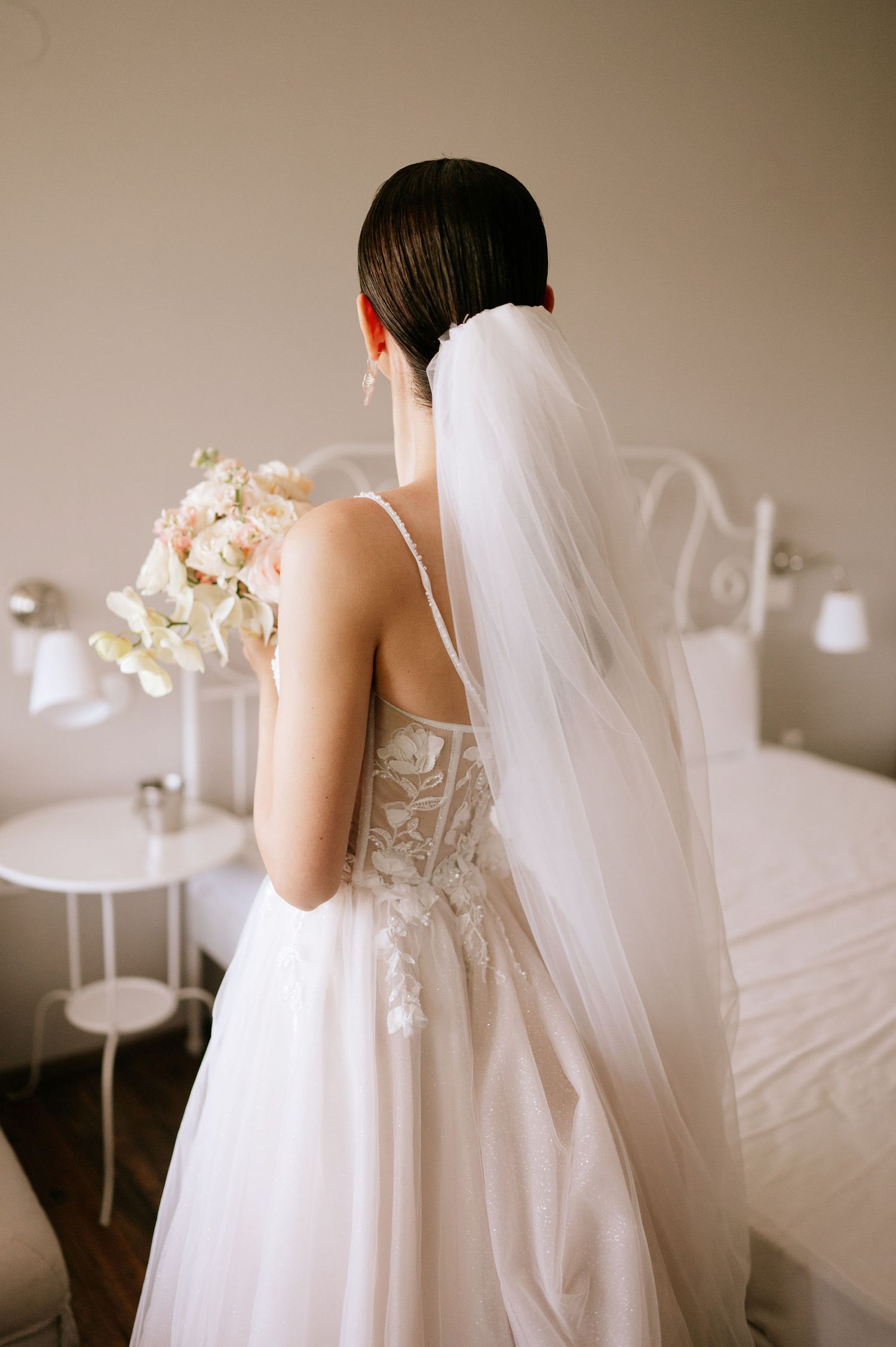 Artistic bridal portrait showing intricate back details of white wedding gown and veil.