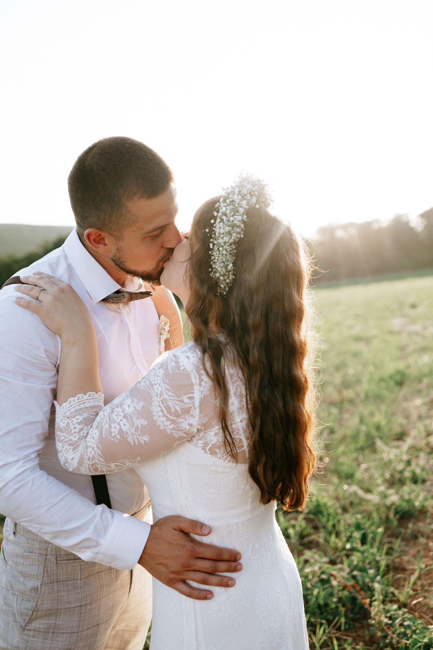 A romantic sunset photoshoot of a couple in wedding attire embracing in a field.
