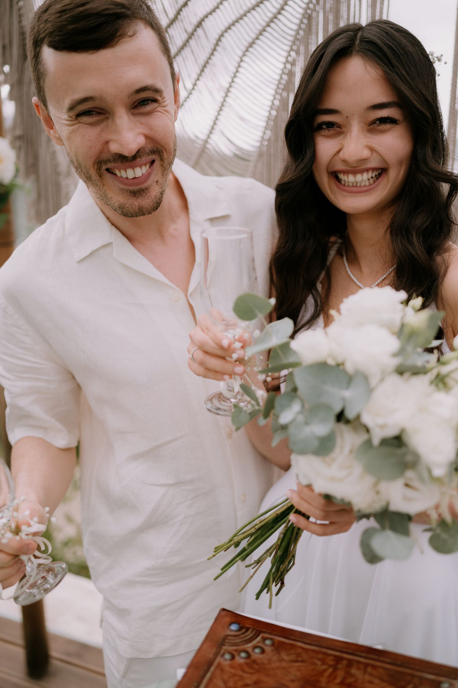 Intimate wedding celebration with couple sharing drinks and smiles near a decorative wooden table.