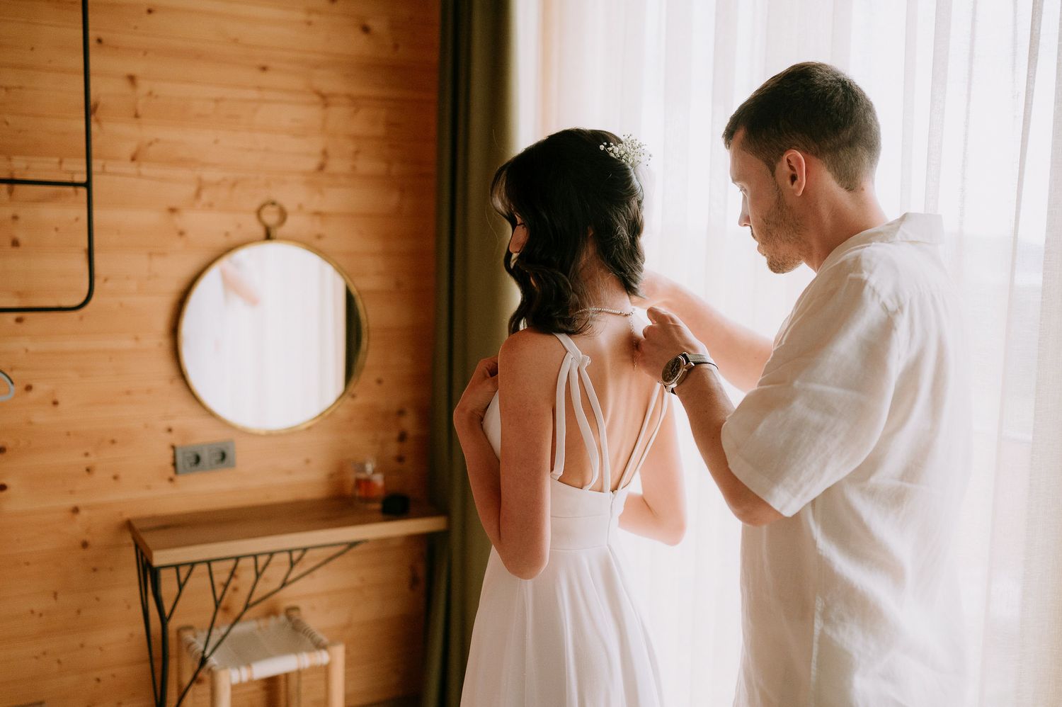 A tender moment captured in a rustic wooden cabin as a couple gets ready on their wedding day.