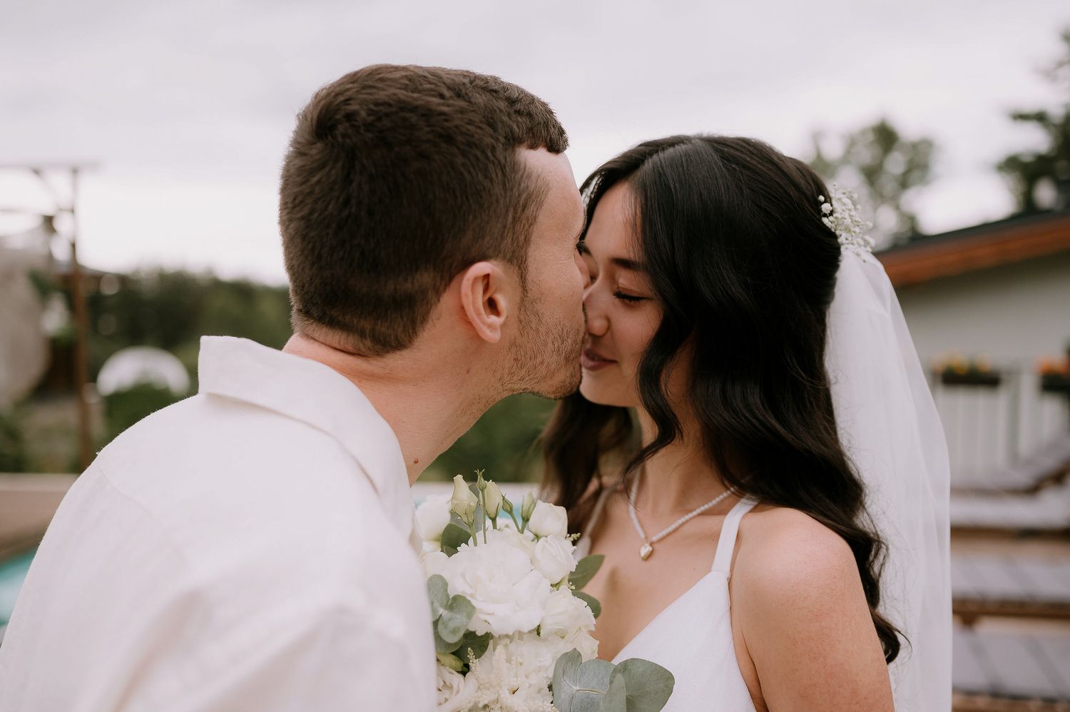 A romantic wedding moment captured by the poolside with flowing white fabric in the background.