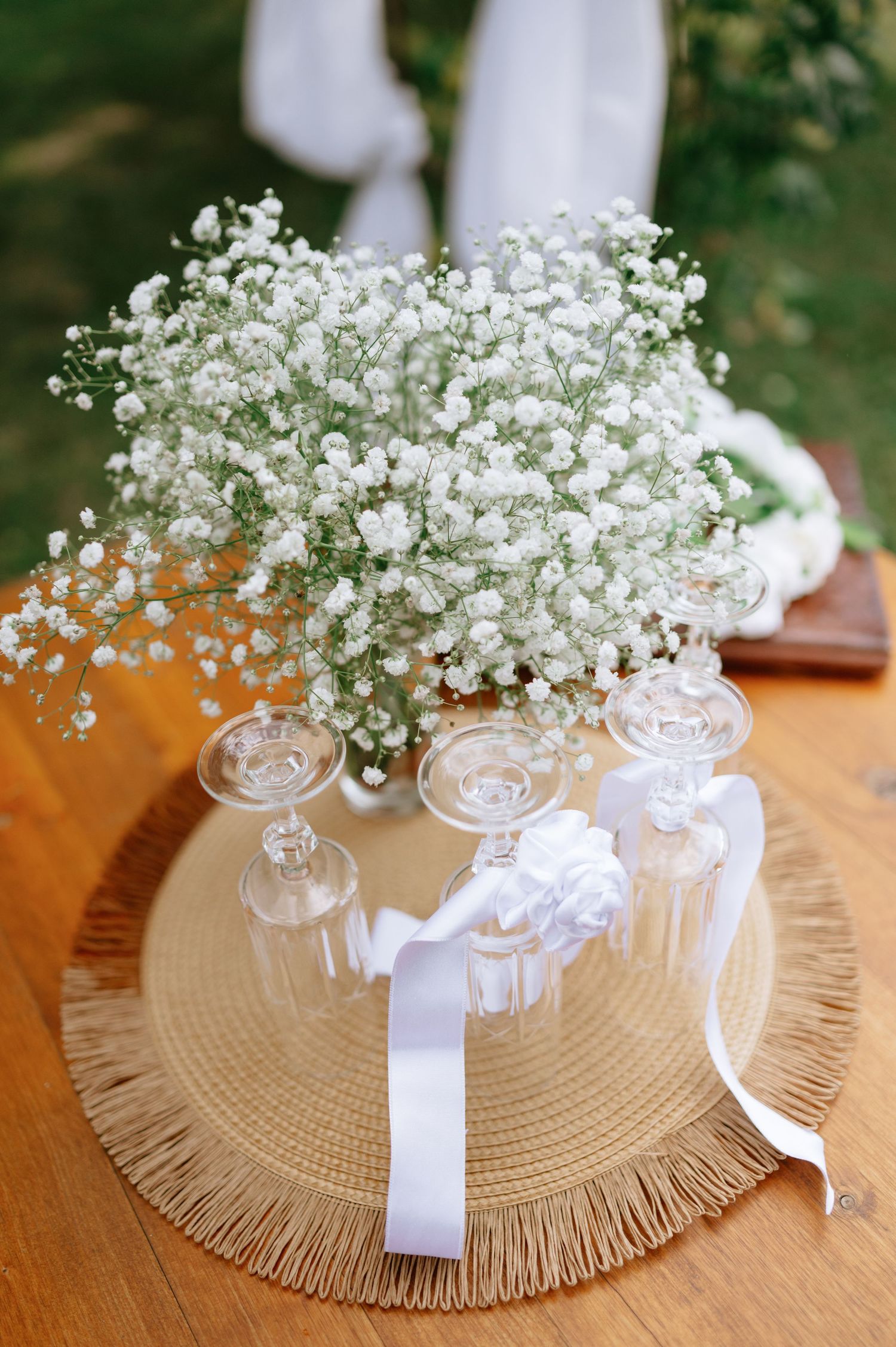 Baby's breath flower arrangement with white ribbon on a woven placemat with wine glasses.