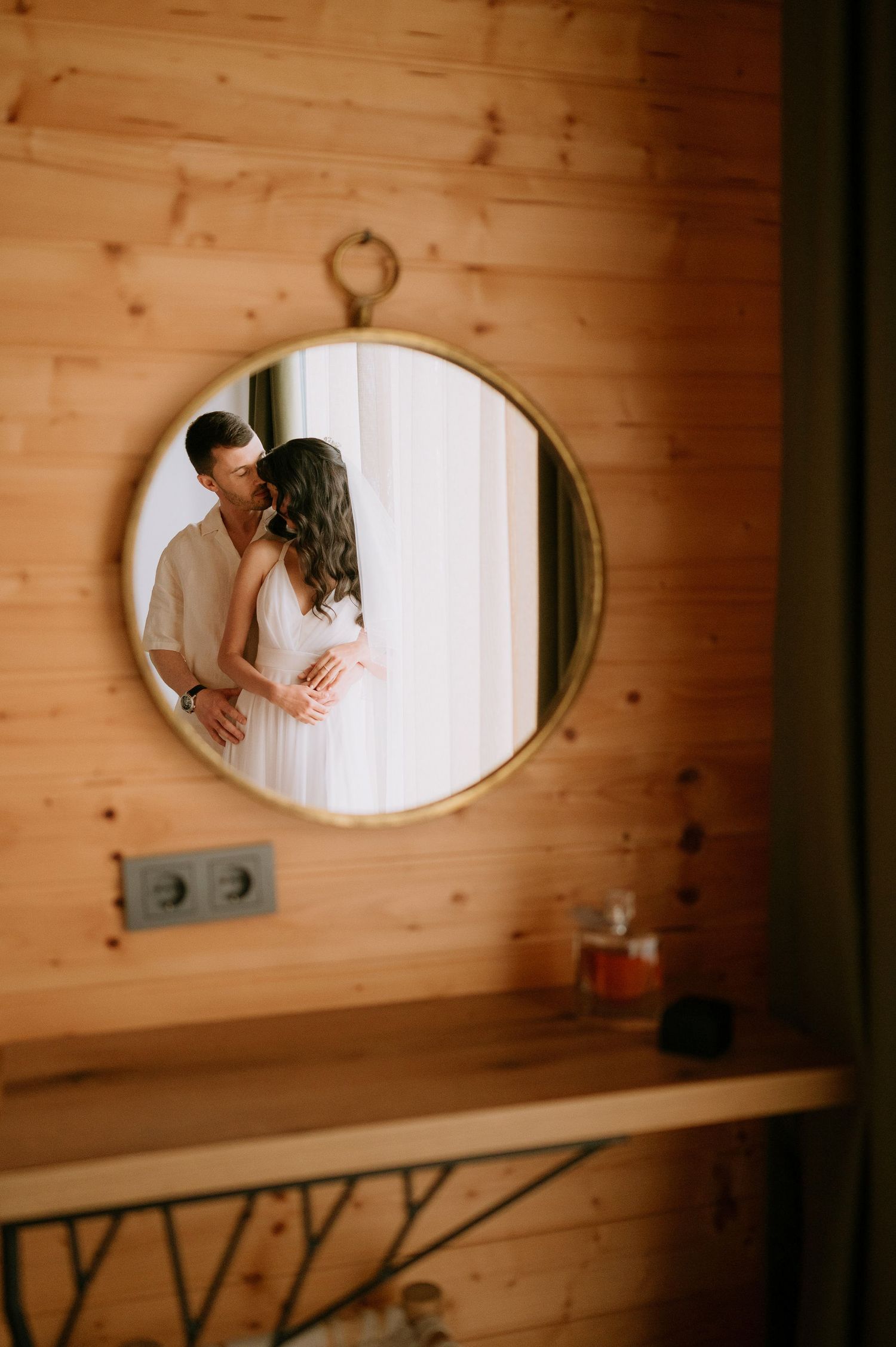 Intimate wedding portrait reflected in a circular mirror against wooden paneled walls.