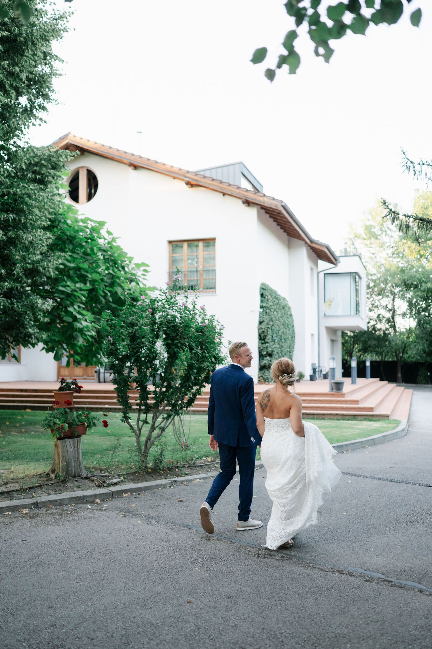 Bride and groom walking away together on path near white house.