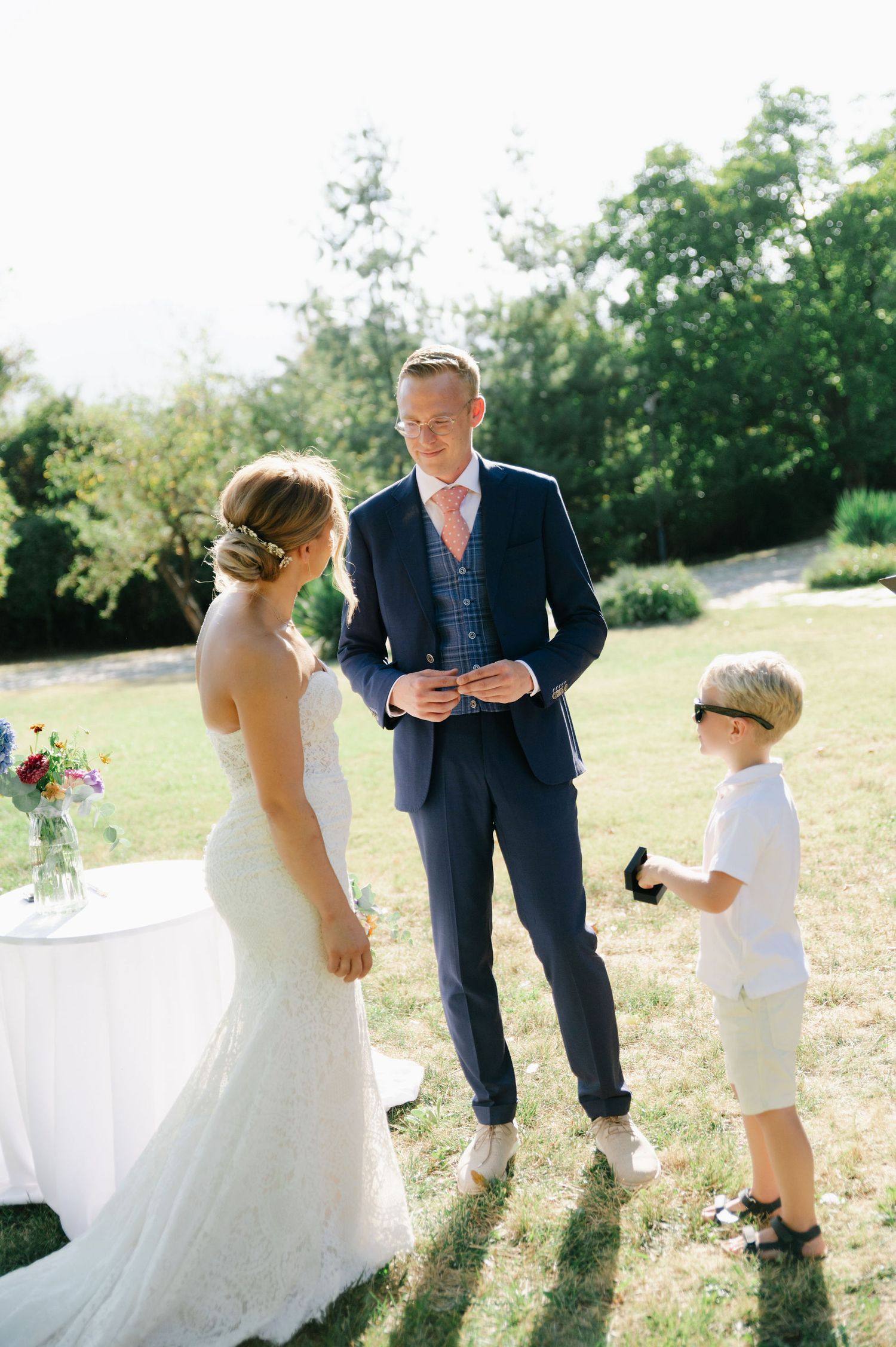 Wedding couple and child interact during outdoor ceremony in natural setting.
