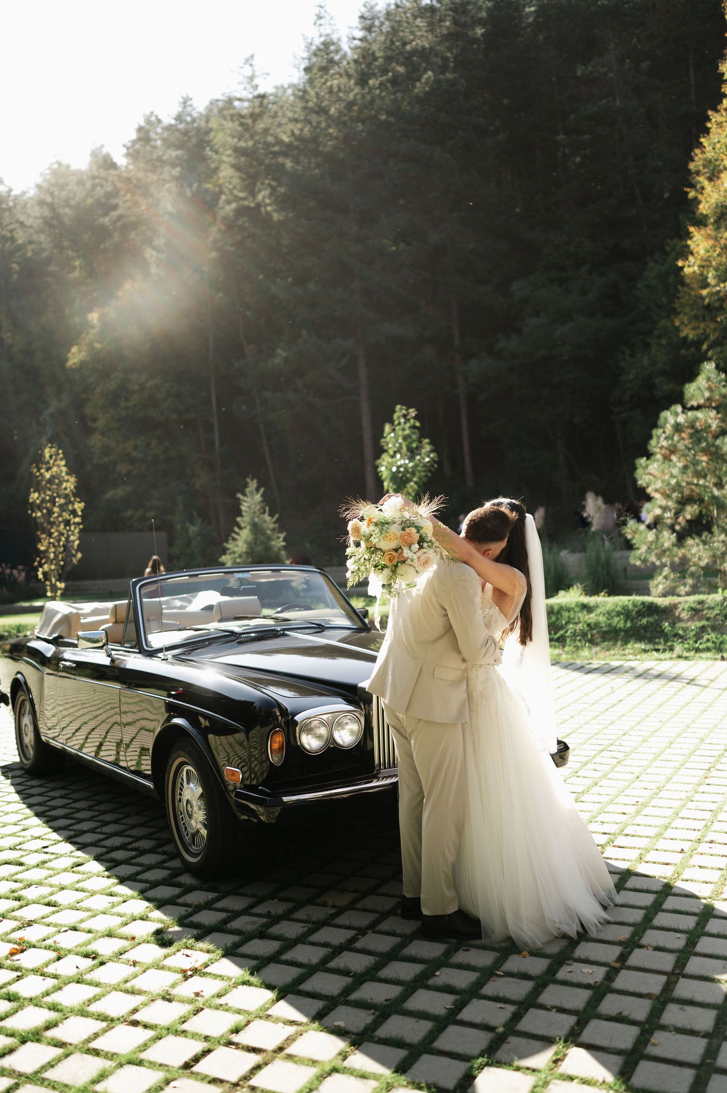 Luxury vintage Rolls Royce parked on geometric paved courtyard during wedding photoshoot.