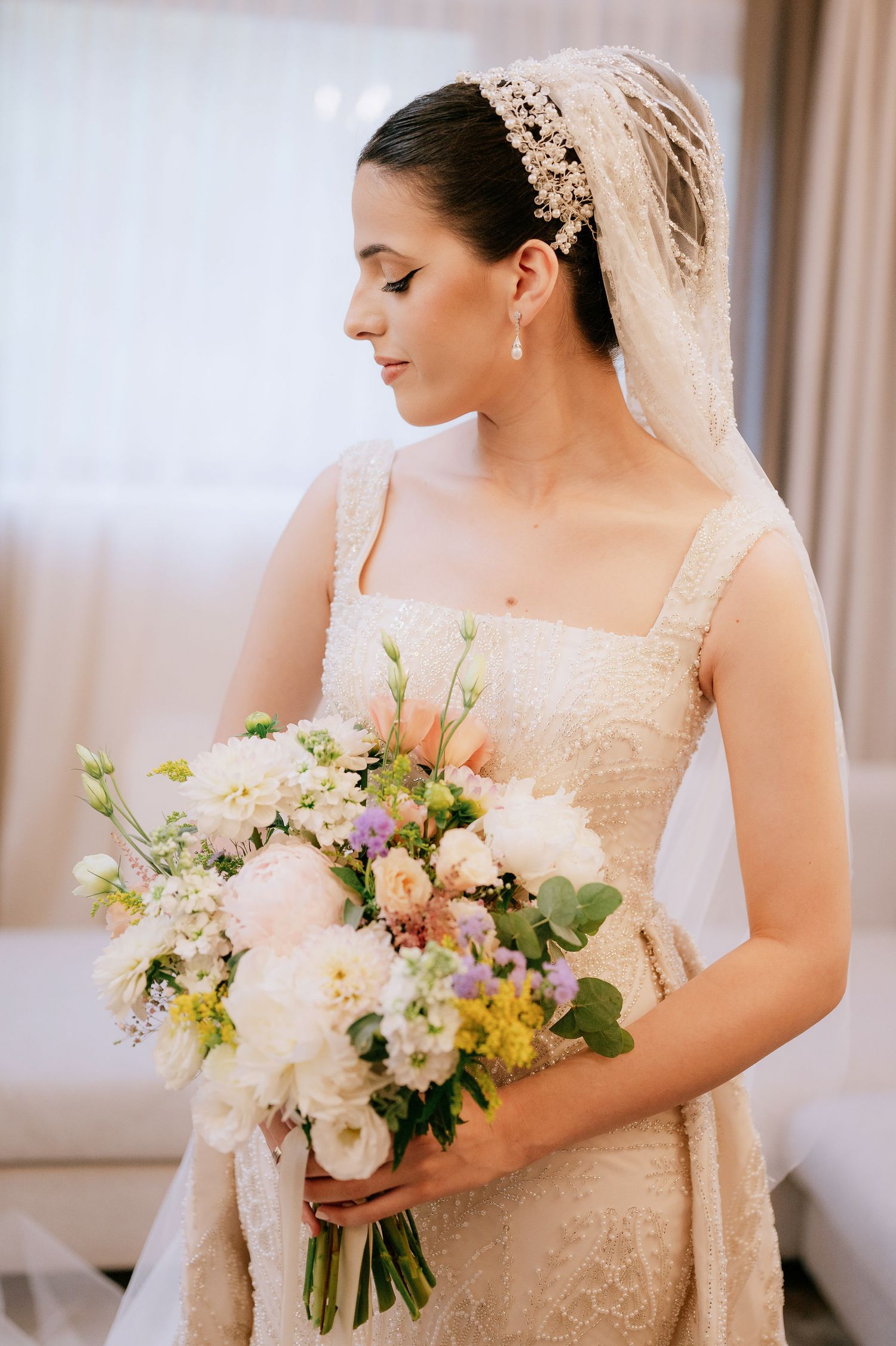 Side view of bride with classic updo wearing pearl headpiece and holding romantic pastel bouquet.