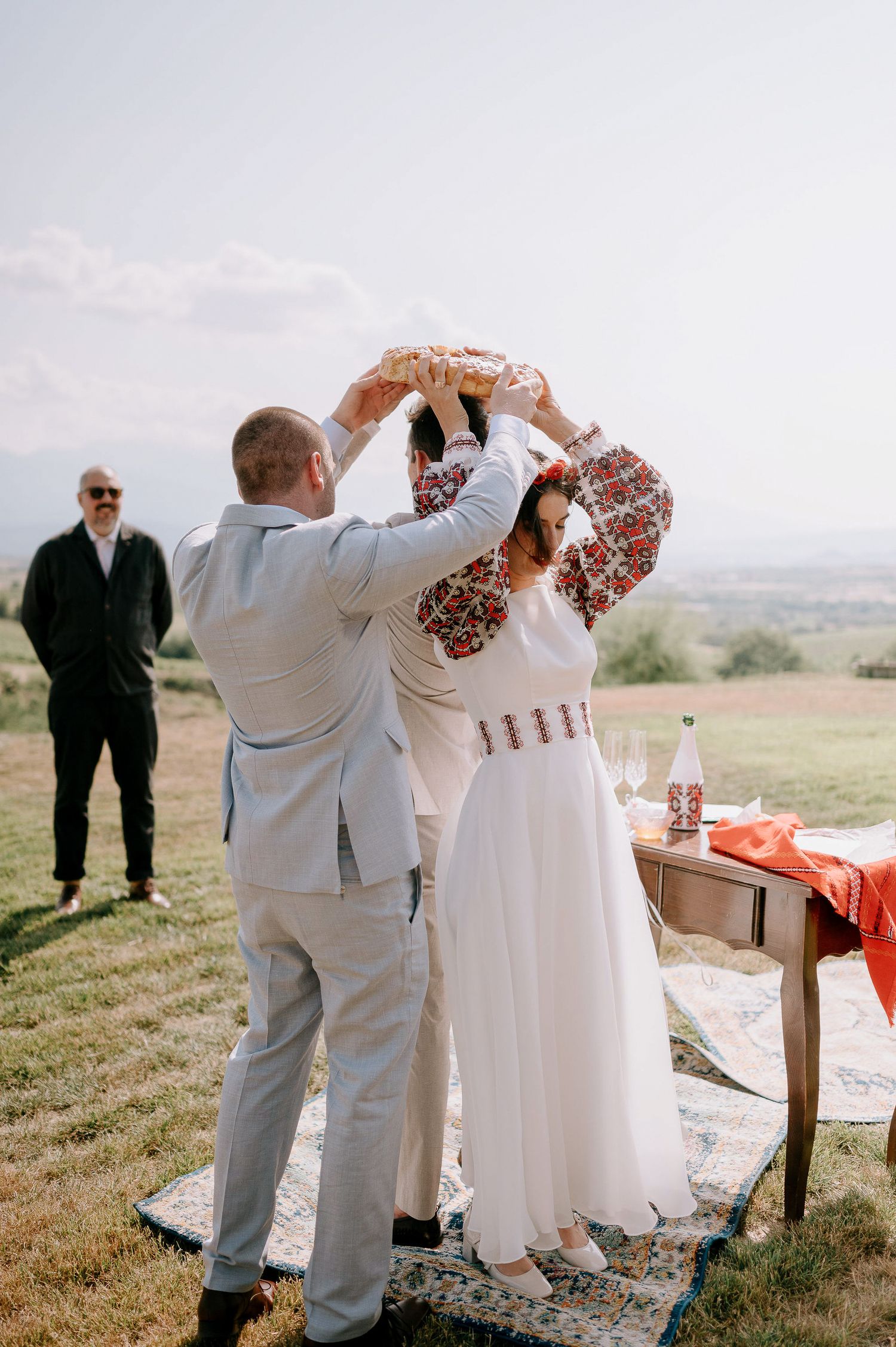 Wedding party in white and beige attire participates in an outdoor ceremony ritual.