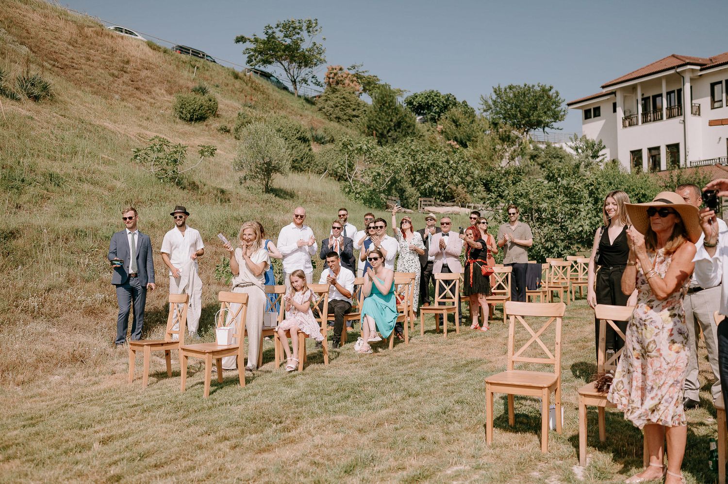 Wedding guests seated on rustic wooden benches during outdoor hillside ceremony.