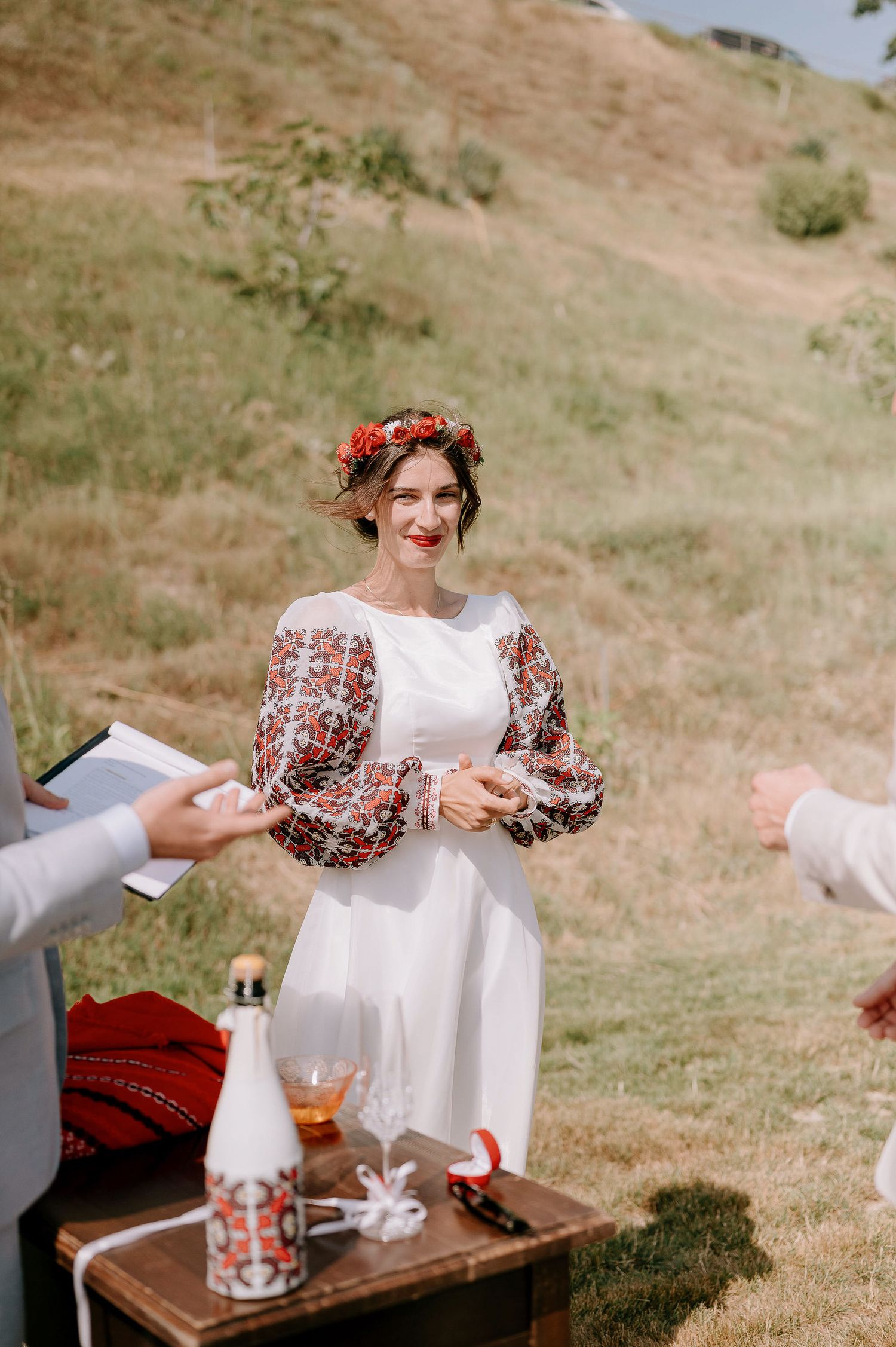 Person in white dress with floral details sitting at outdoor table.