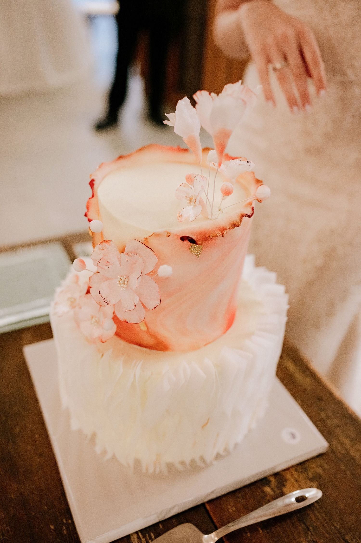 Elegant white wedding cake with coral-colored accents displayed on a rustic wooden table.