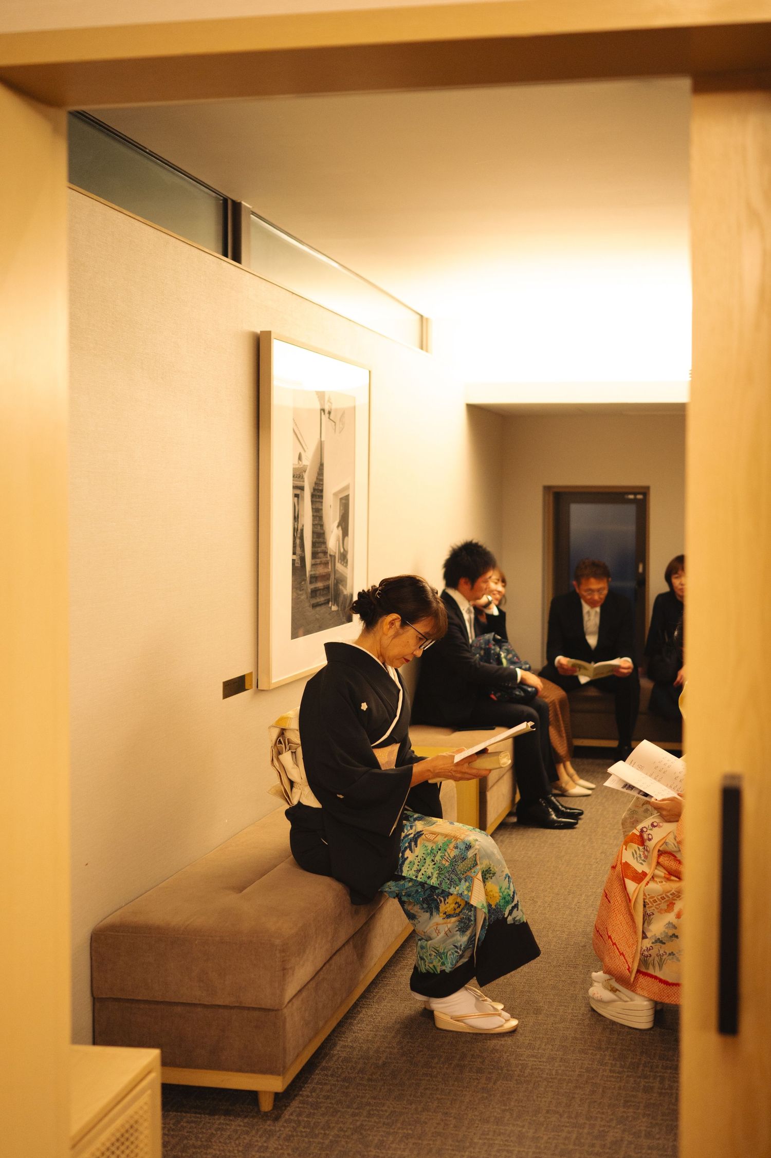 Wedding guests relax in a hallway lounge area with beige walls and comfortable seating.