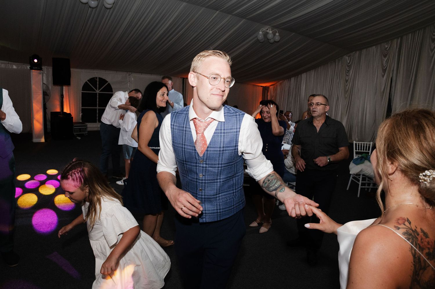 People dancing and socializing at a dimly lit indoor wedding reception venue.