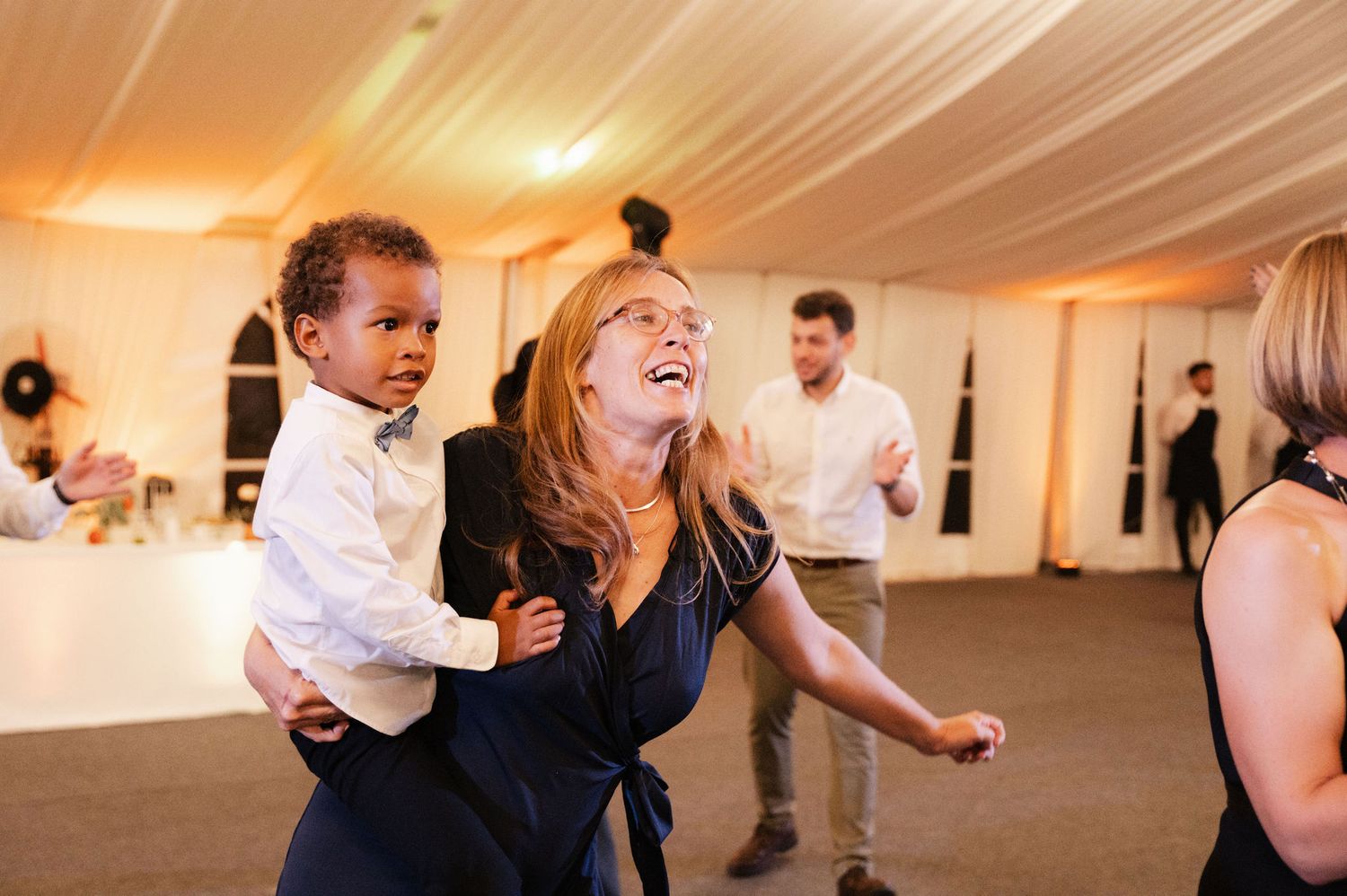 Wedding guests dance and celebrate together on the dance floor at an indoor reception venue with warm lighting.