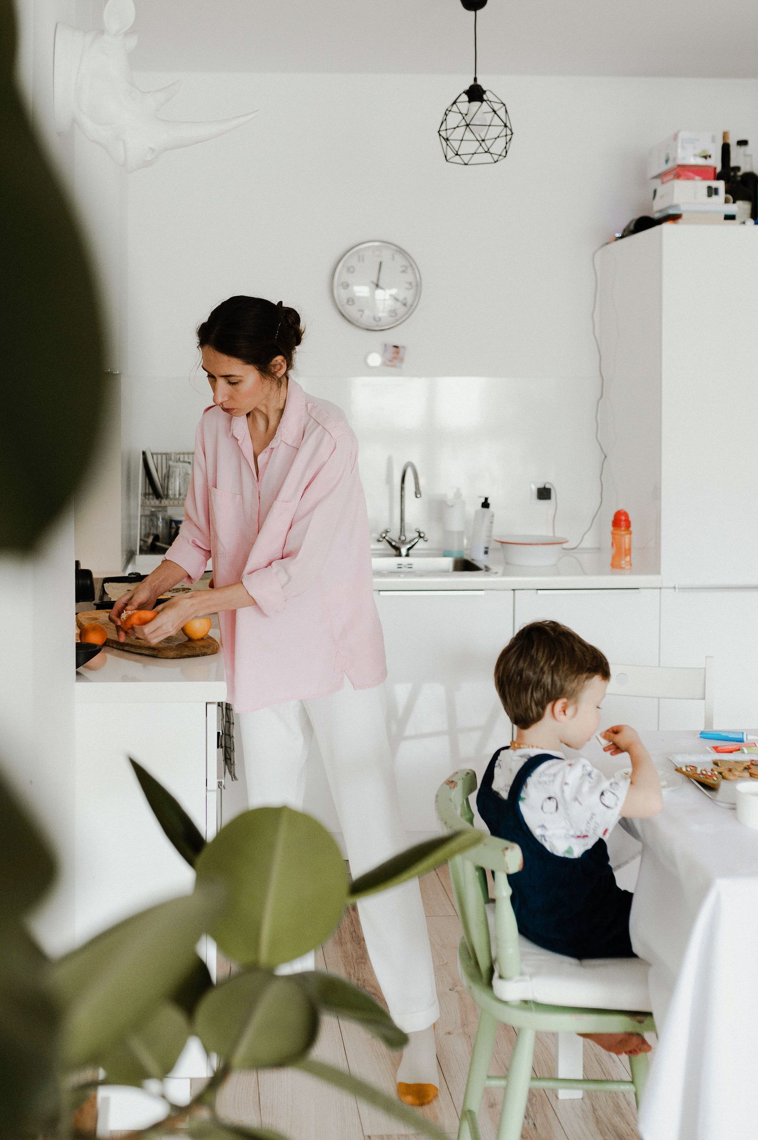 A person in pink attire works at a bright white kitchen counter while interacting with someone seated at the counter.