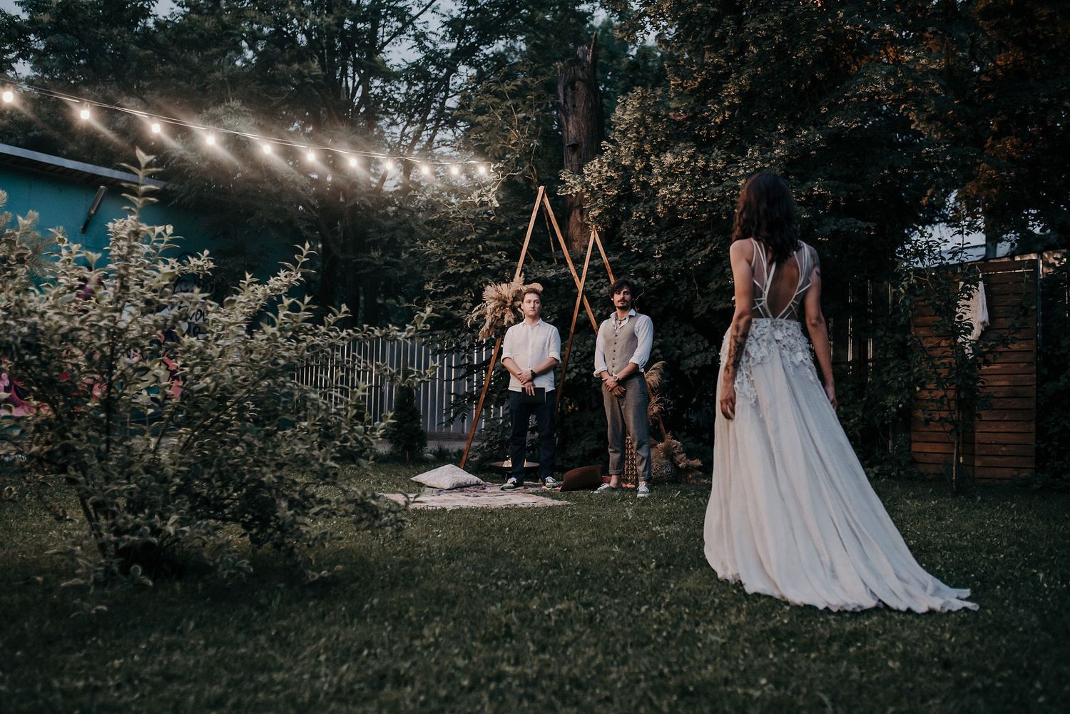Wedding guests gather outdoors at dusk under string lights during an evening garden reception celebration.