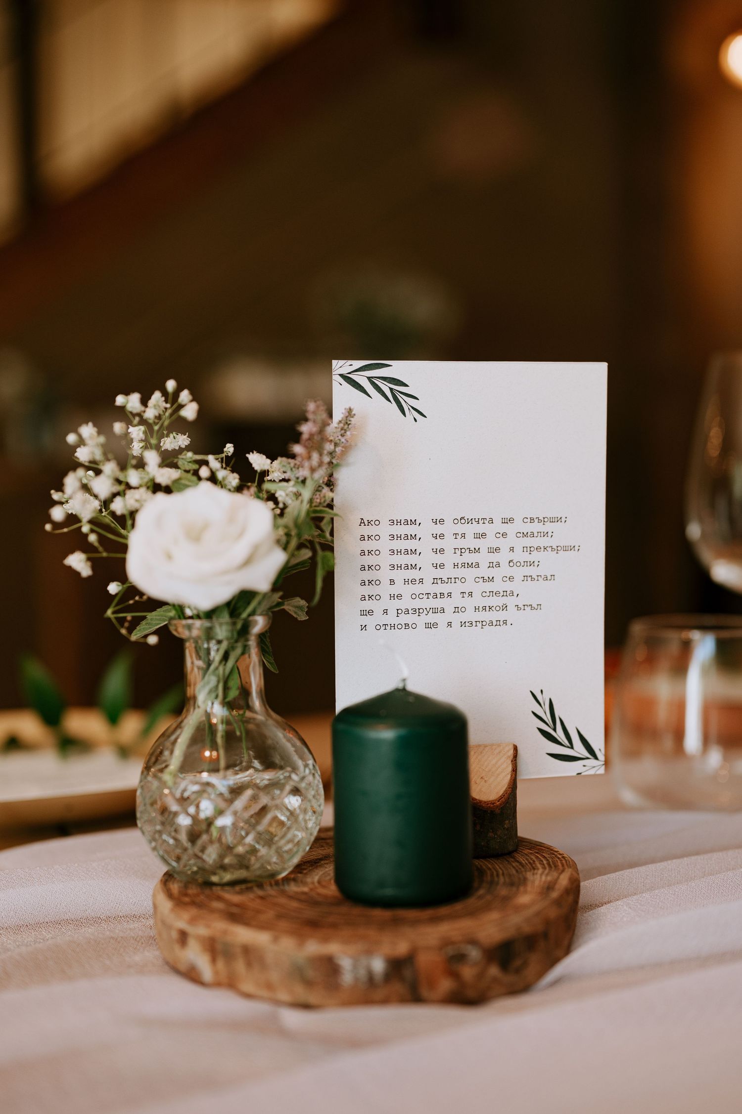Wedding table decor featuring white rose, menu card and green candle on wooden slice.