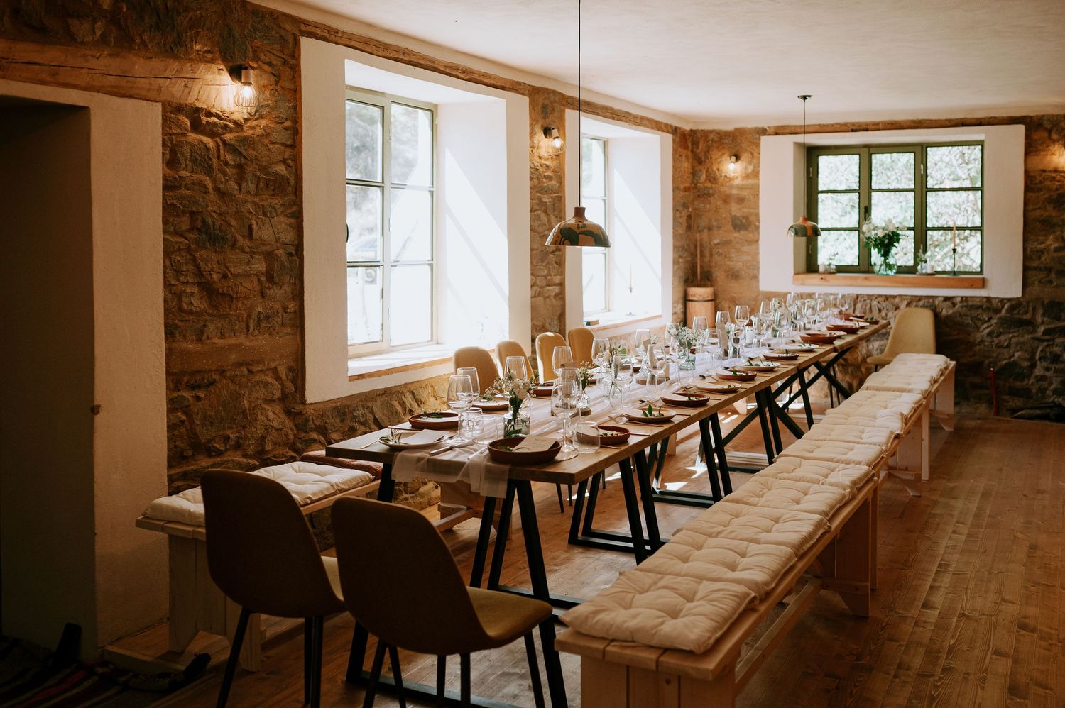 Wide-angle shot of a dining room featuring wooden tables and stone walls with multiple windows.