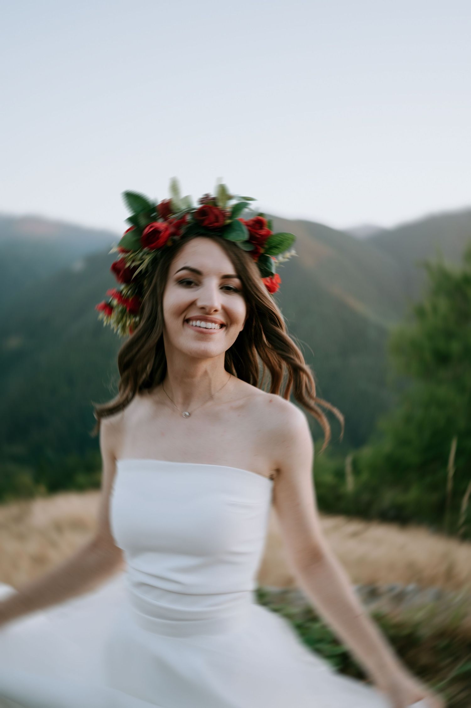 Dancing in a strapless wedding dress with red floral crown against mountain backdrop.