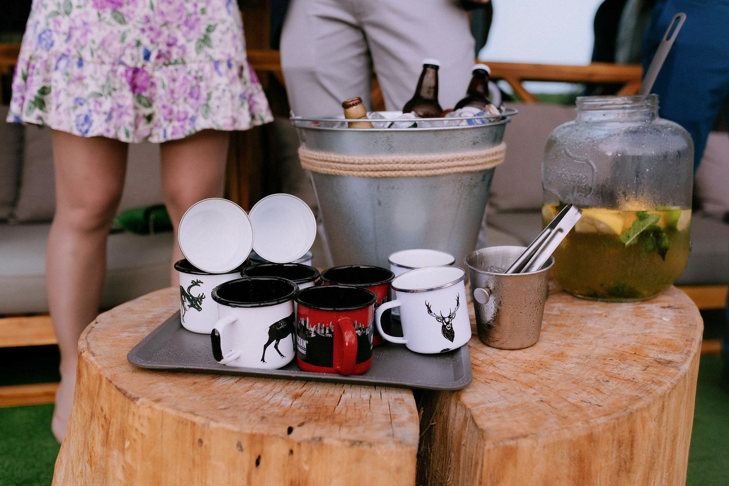 White coffee mugs arranged on a wooden surface at an outdoor event.