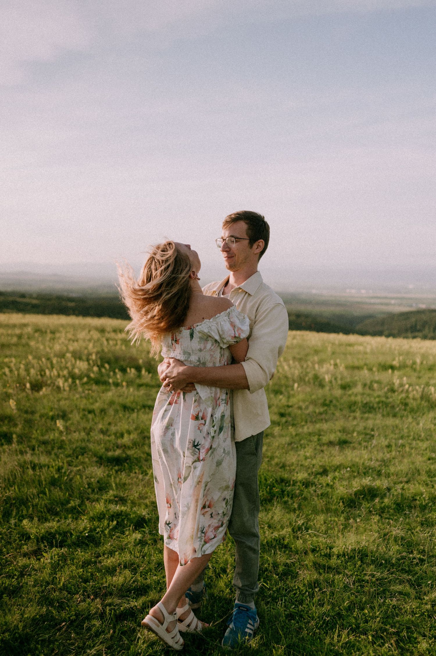 Couple playfully dancing in green field during golden hour photography session.