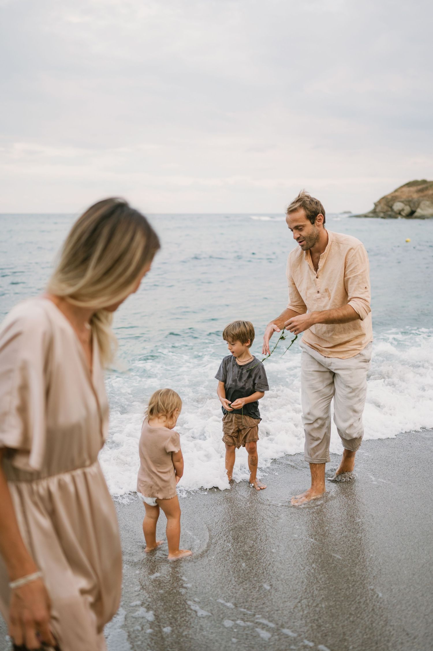 Family of four enjoying a beach day, with parents and two young children playing at the ocean shoreline.