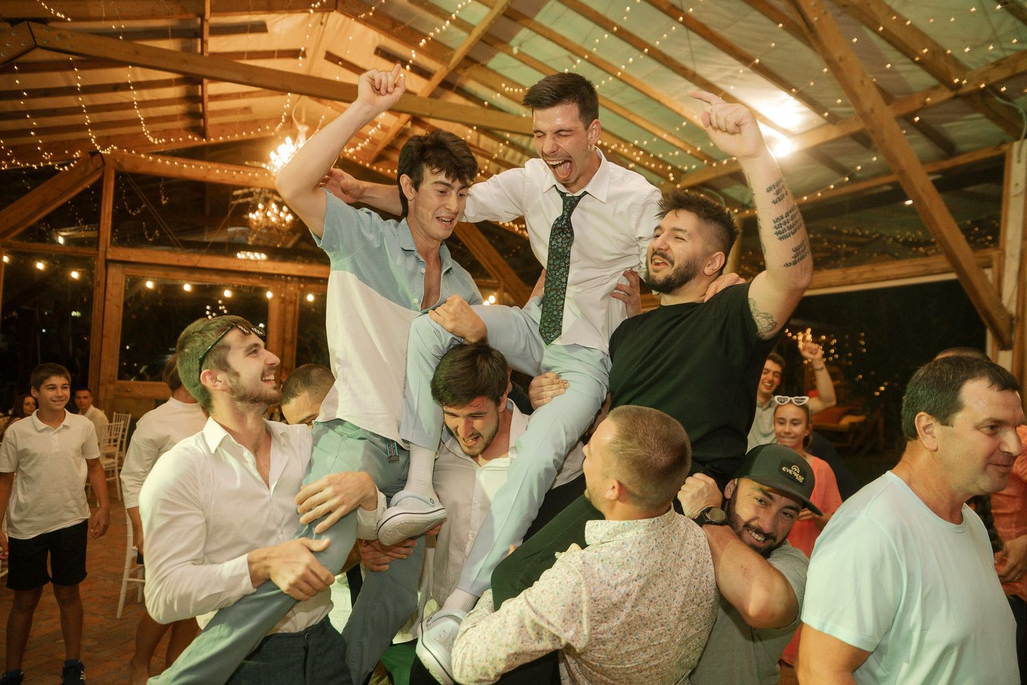 Guests dancing and celebrating at a rustic indoor wedding reception venue with wooden beams and string lights.