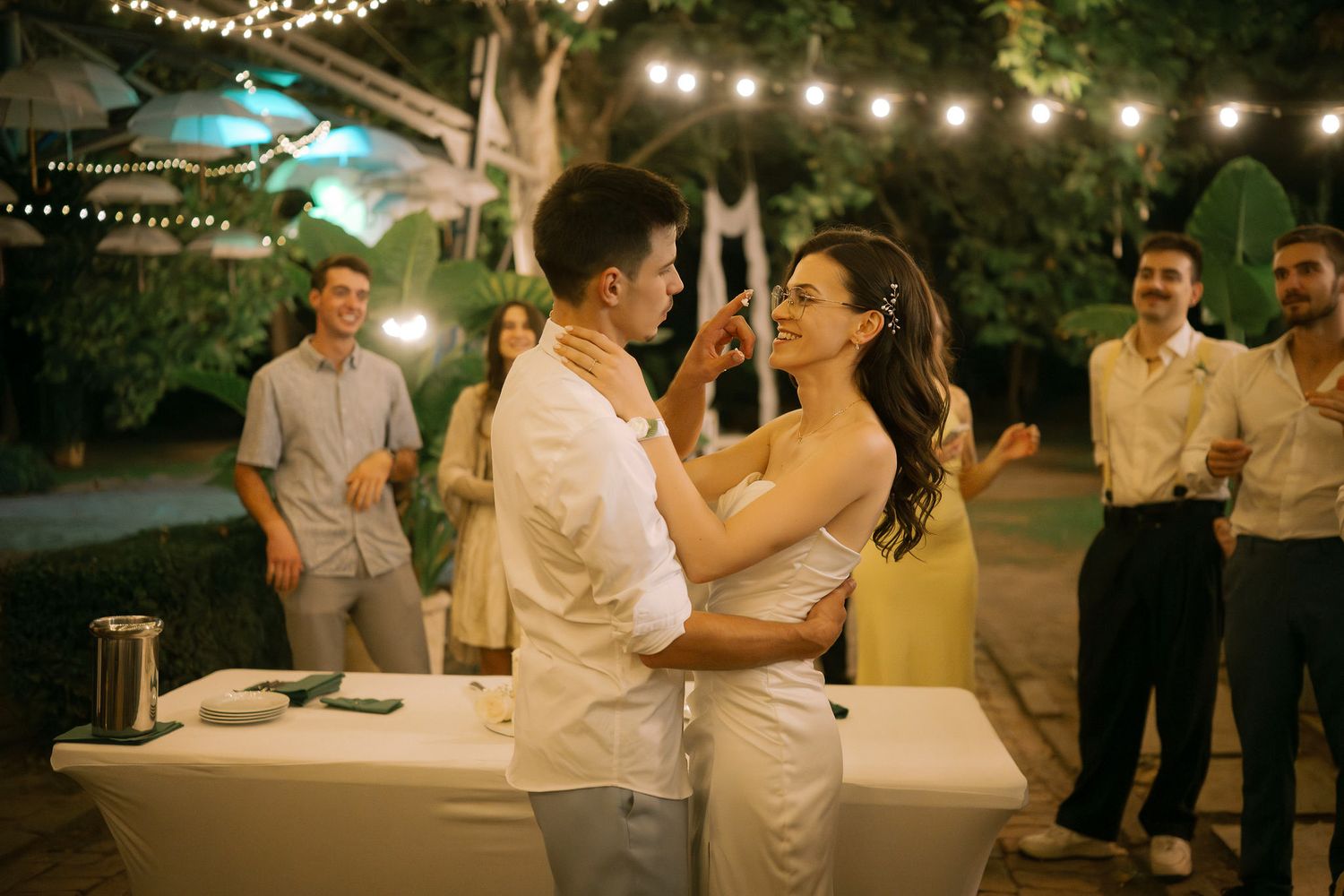 Romantic evening outdoor wedding reception with string lights illuminating couples dancing and celebrating.