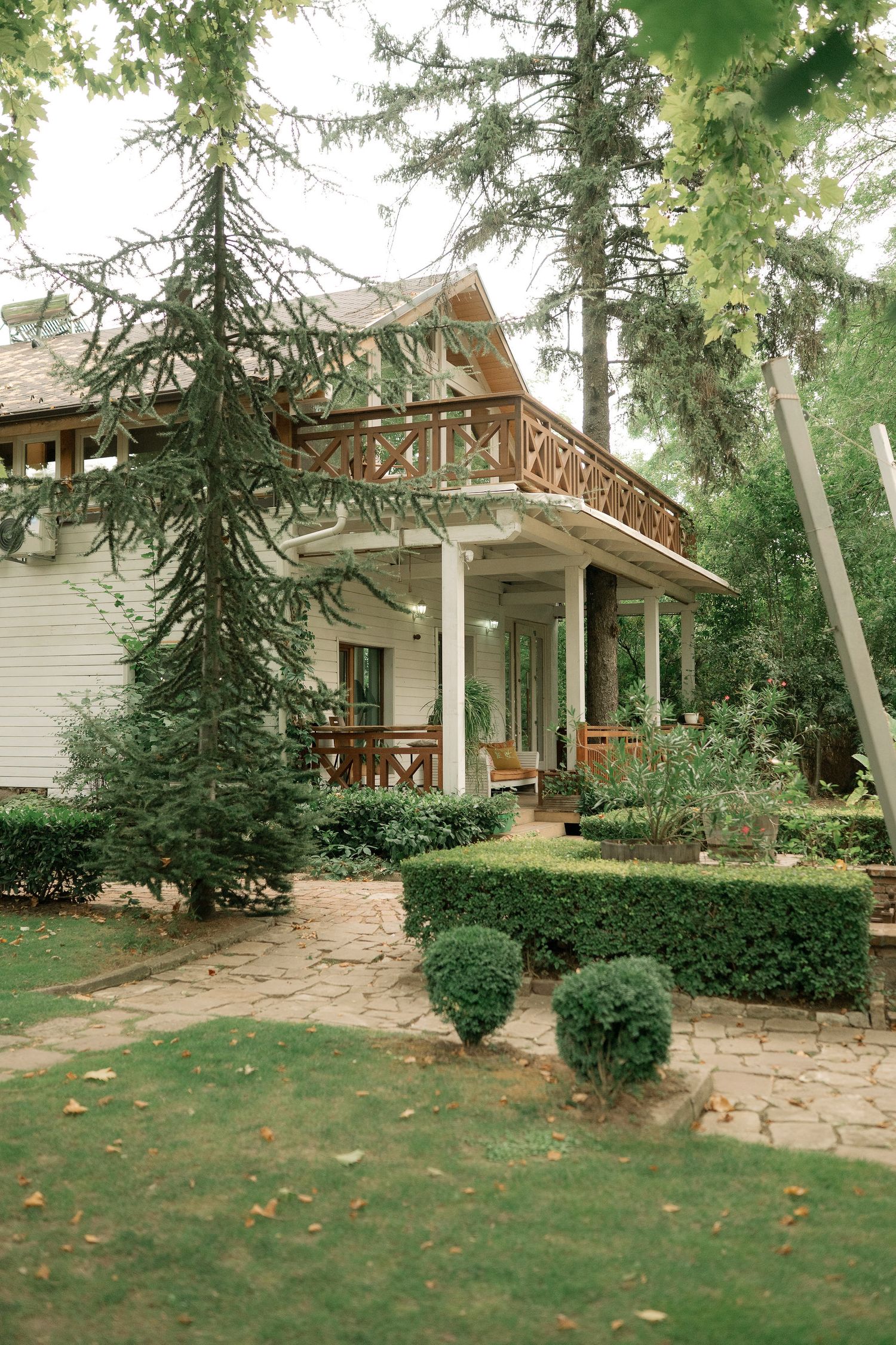 Panoramic view of a rustic wooden house with evergreen trees and landscaped lawn in a tranquil outdoor setting.