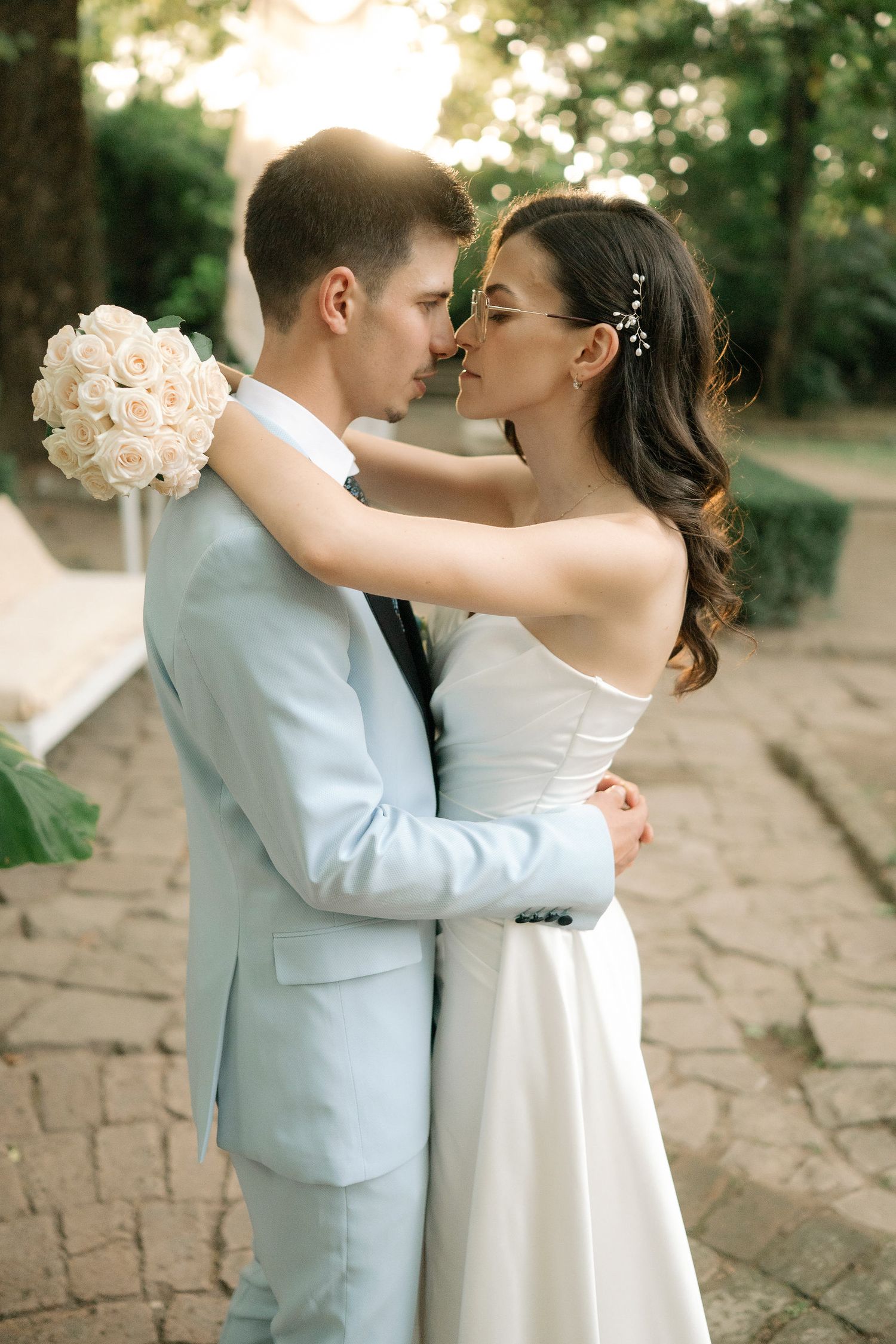 A romantic wedding couple shares intimate moments on a stone pathway surrounded by greenery.