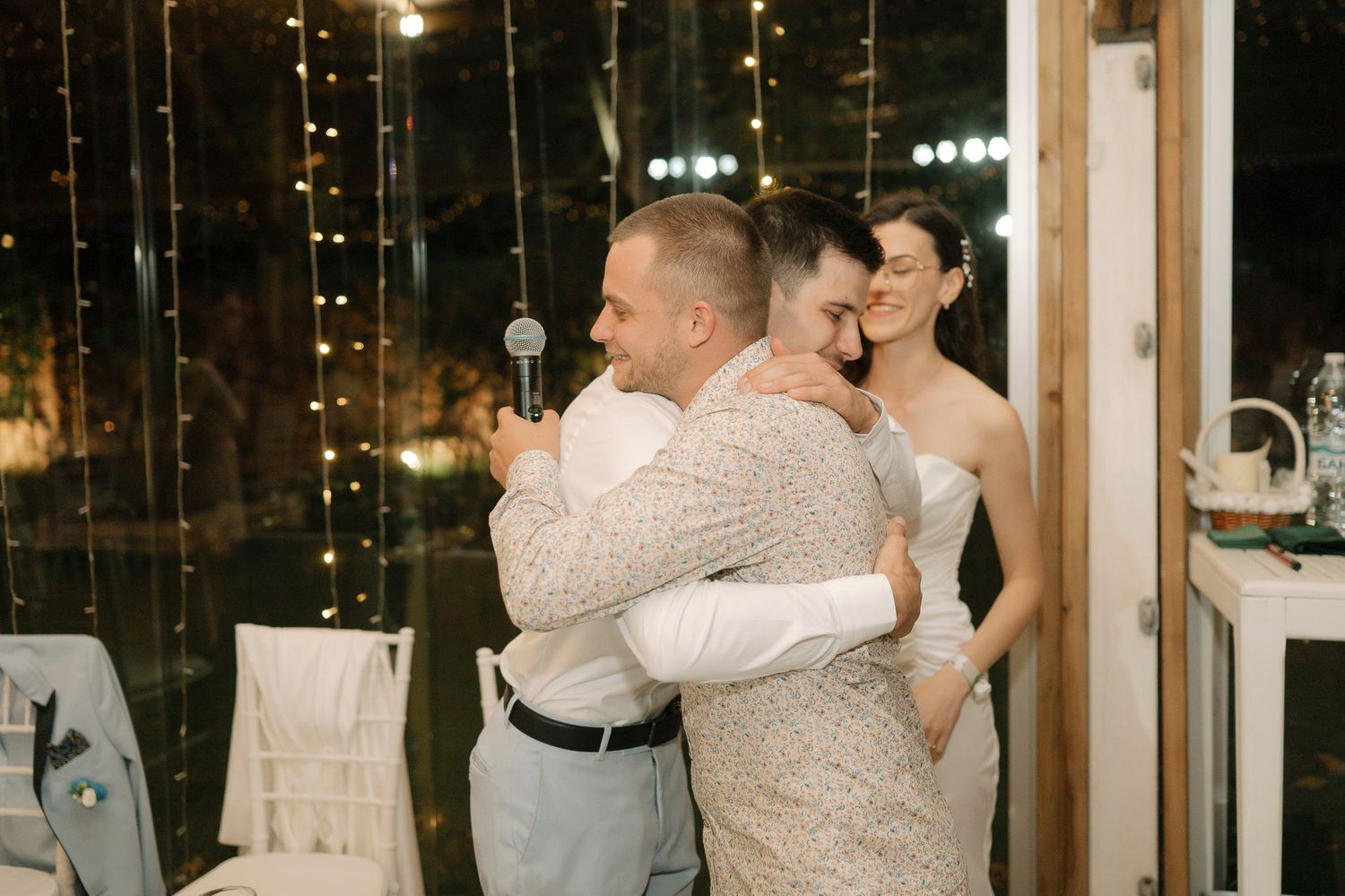 A couple shares a romantic dance during their wedding reception in a warmly lit venue with large windows.