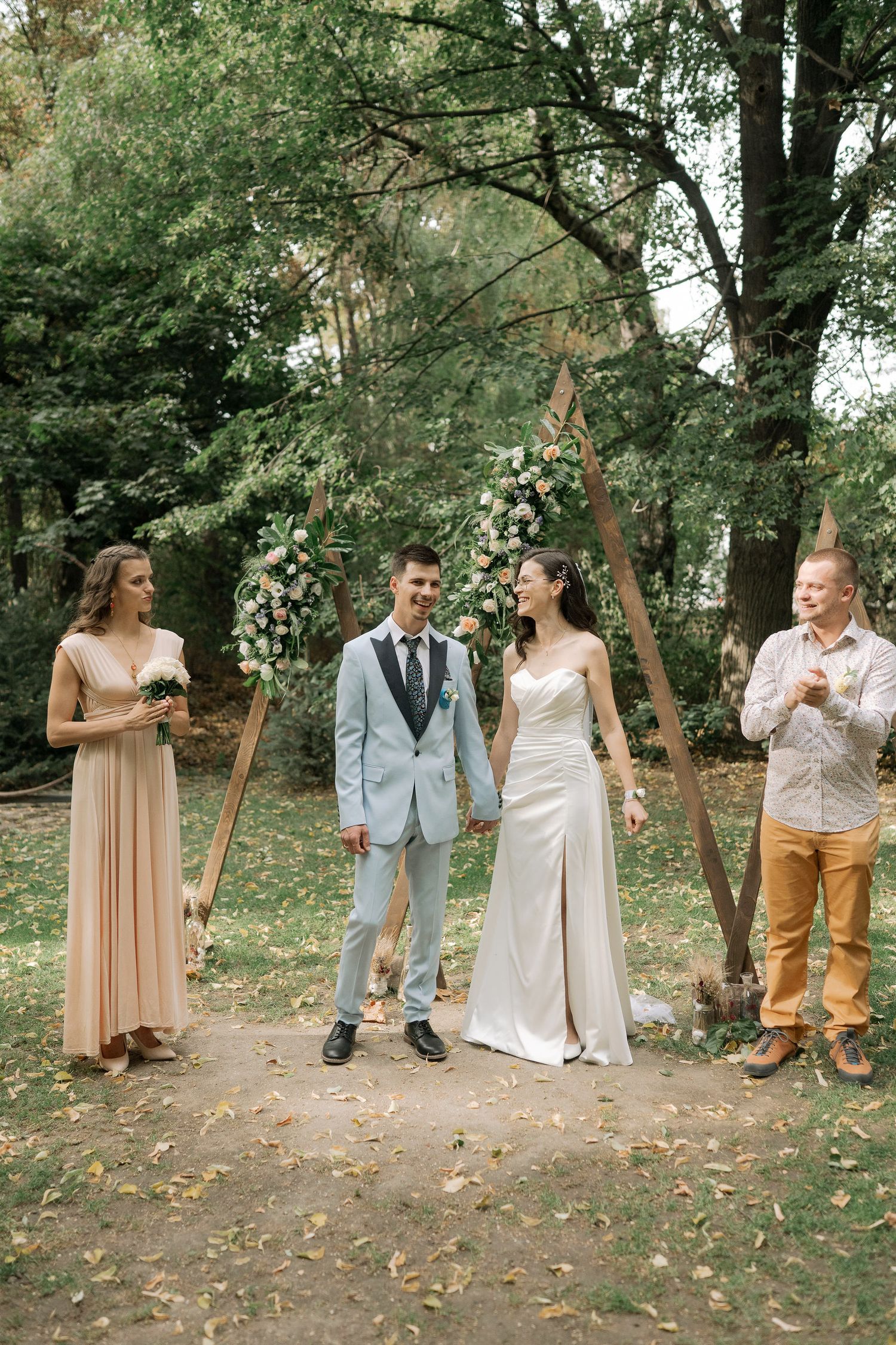 A wedding party enjoys a playful moment in a wooded outdoor setting during a photo session.