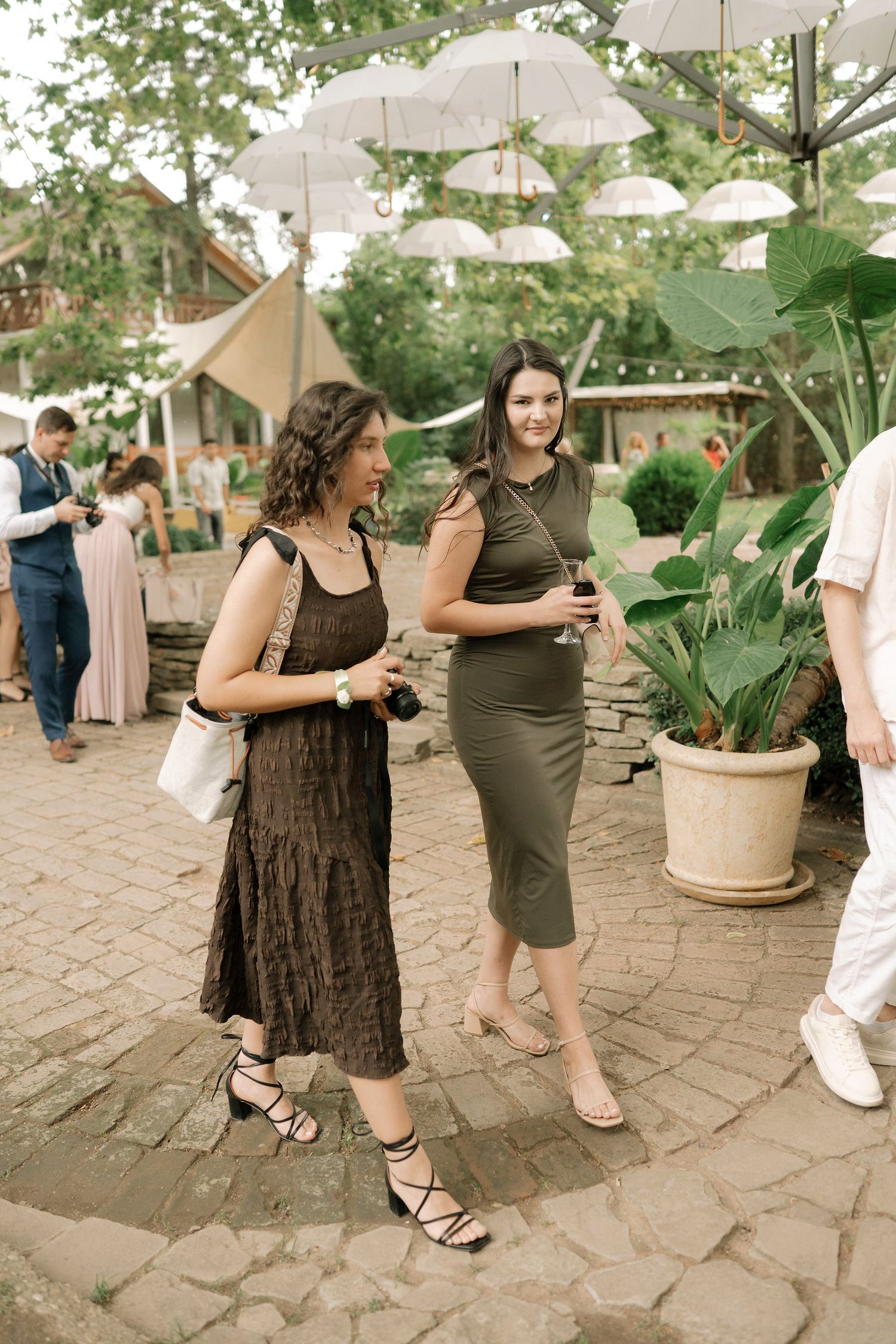 People gather outdoors under white umbrellas on a stone patio during a social event.