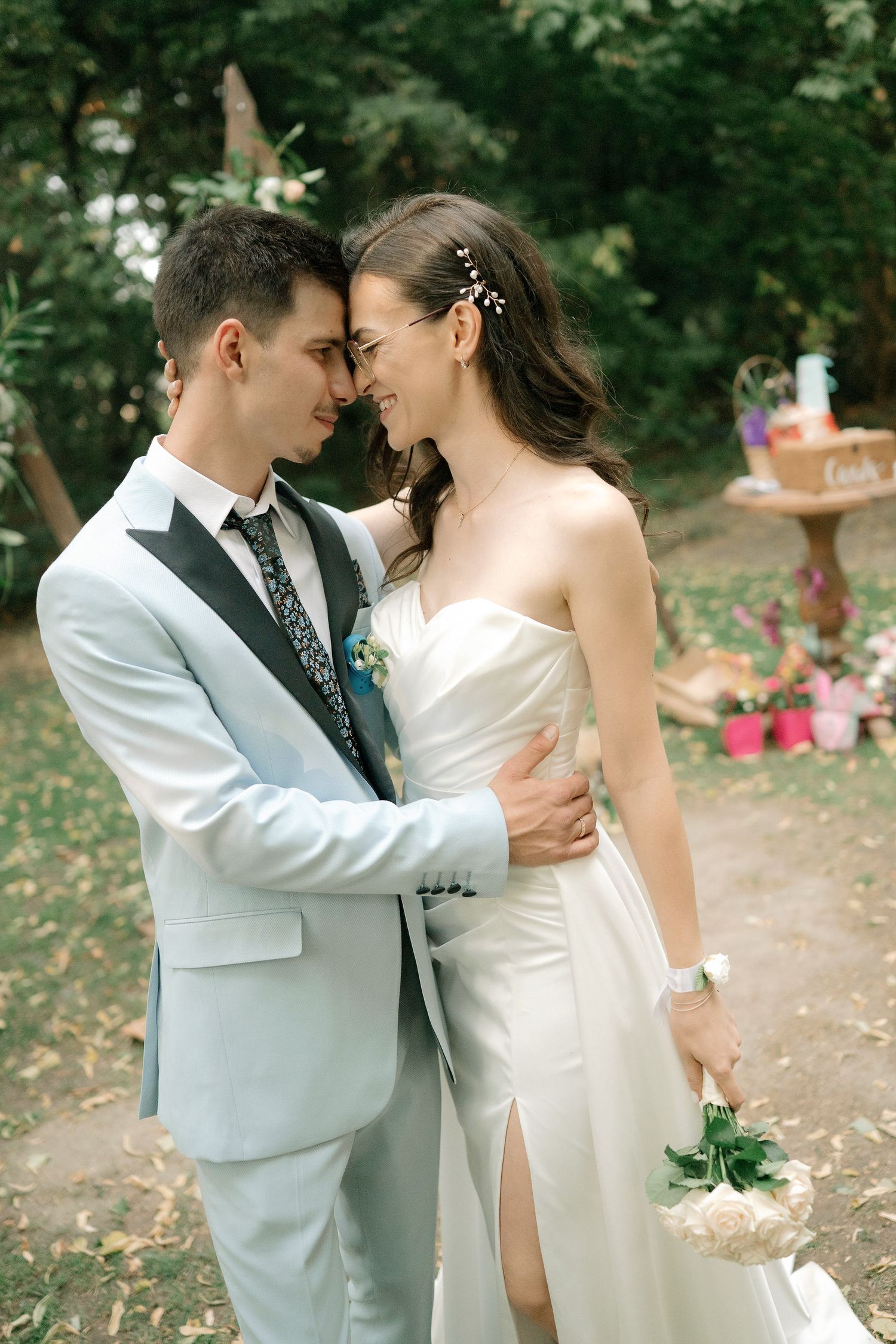 A romantic wedding couple shares an intimate moment in a garden setting wearing white and gray formal attire.