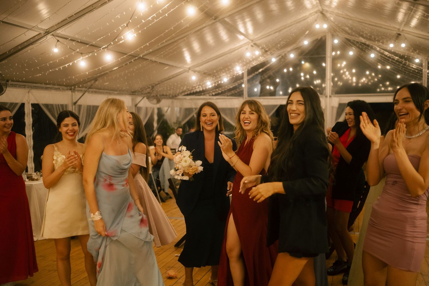 Guests enjoying themselves at a lively wedding reception under string lights in a tent venue.
