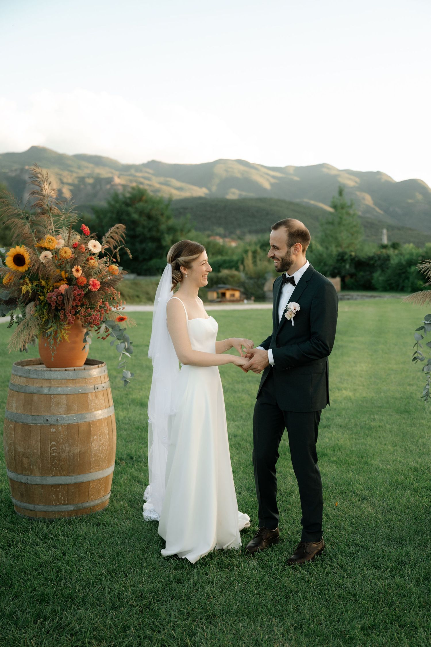 Newlyweds share an intimate moment against mountain backdrop with autumn floral arrangement on wine barrel.